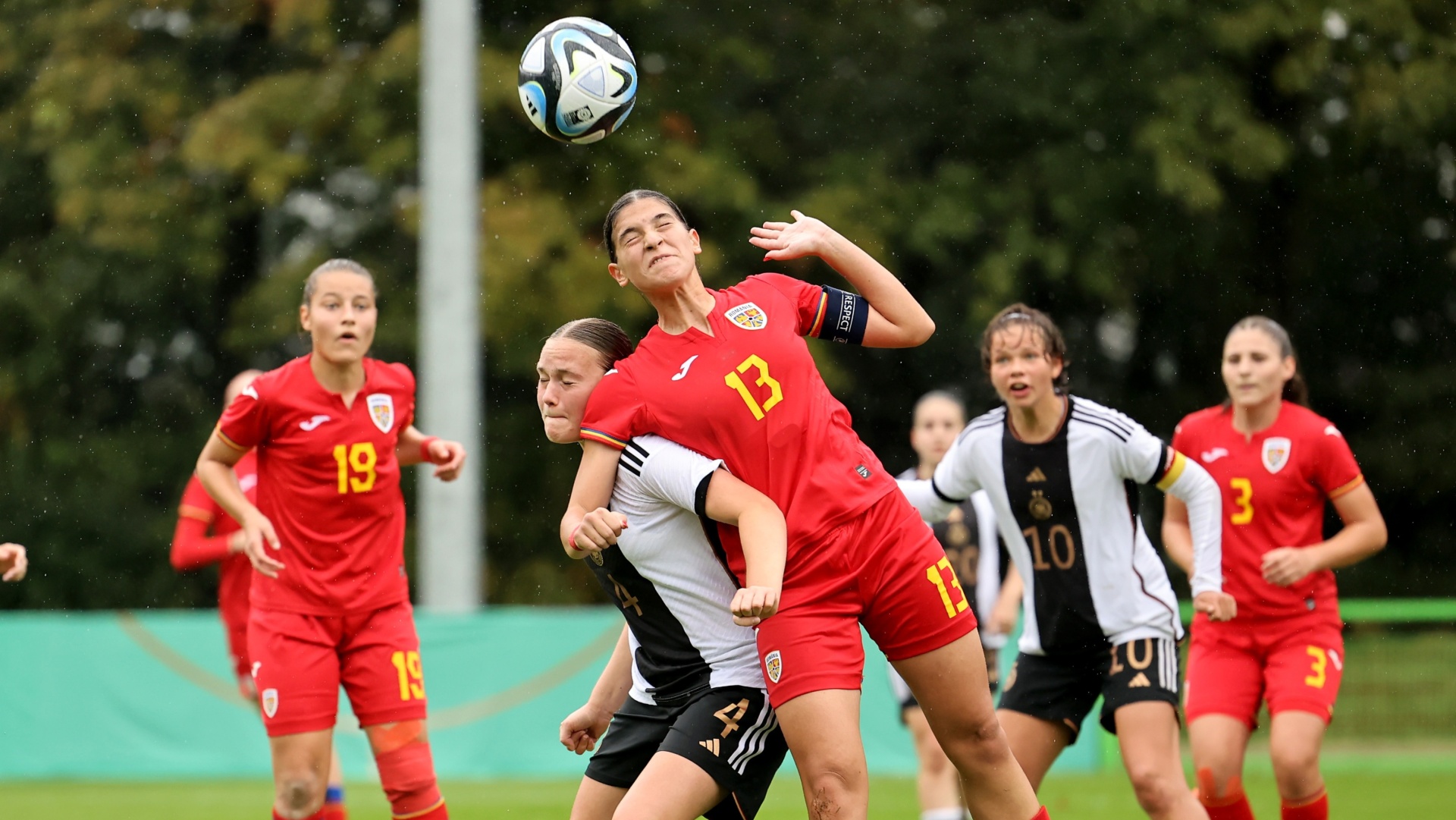 [{"clang_id":1,"value":"Zwei Fußballspielerinnen kämpfen um den Ball. Eine trägt rot mit der Nummer 13, die andere schwarz-weiß mit der Nummer 4. Im Hintergrund weitere Spielerinnen."}]