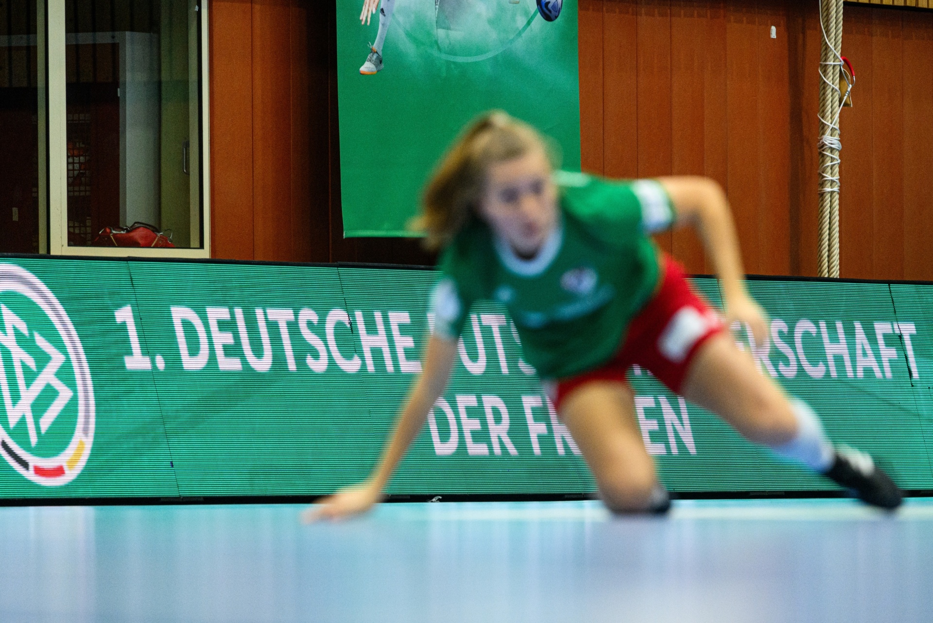 [{"clang_id":1,"value":"Sportler in Bewegung vor einer grünen Werbetafel mit Text \"1. Deutsche ...schaft der Frauen\". Im Hintergrund eine Sporthalle."}]