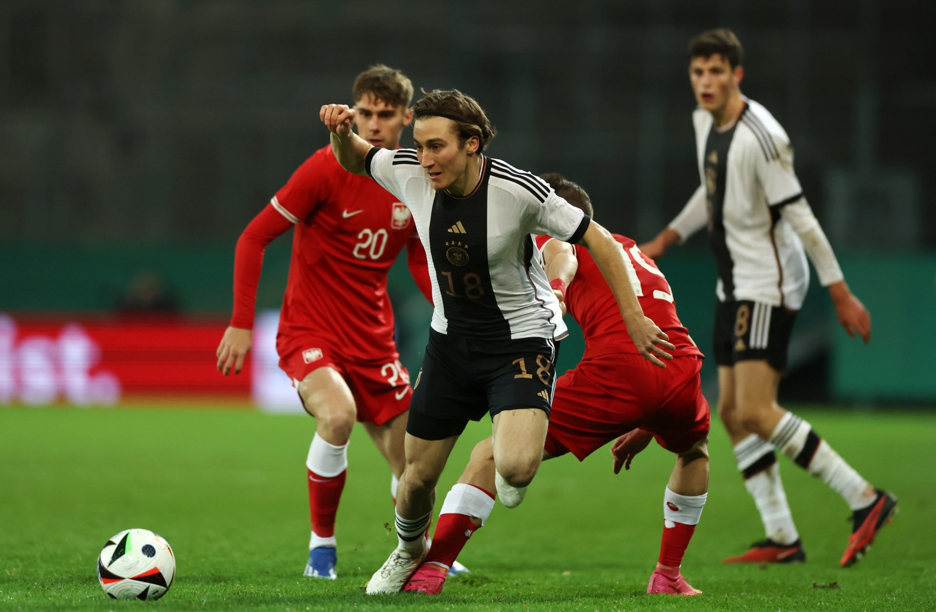 [{"clang_id":1,"value":"Fußballspiel: Spieler in schwarz-weiß-Trikots mit Nummer 18 und rot-weißen Trikots kämpfen um den Ball auf grünem Rasen. Im Hintergrund weitere Spieler."}]