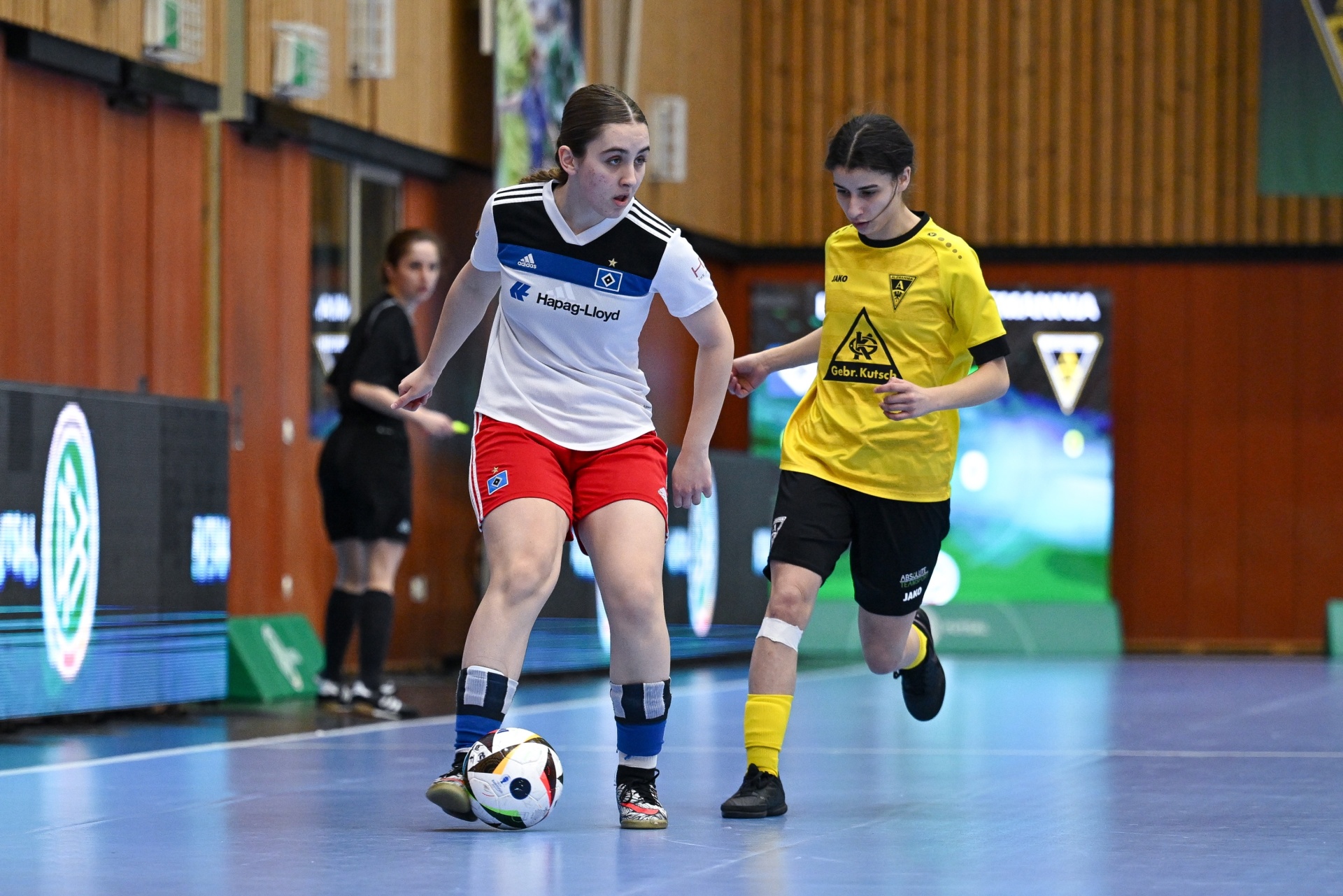 [{"clang_id":1,"value":"Zwei Futsalspielerinnen in Hallensportanlage. Links: Weißes Trikot mit roten Shorts, dribbelt den Ball. Rechts: Schwarzes Trikot mit gelben Akzenten."}]