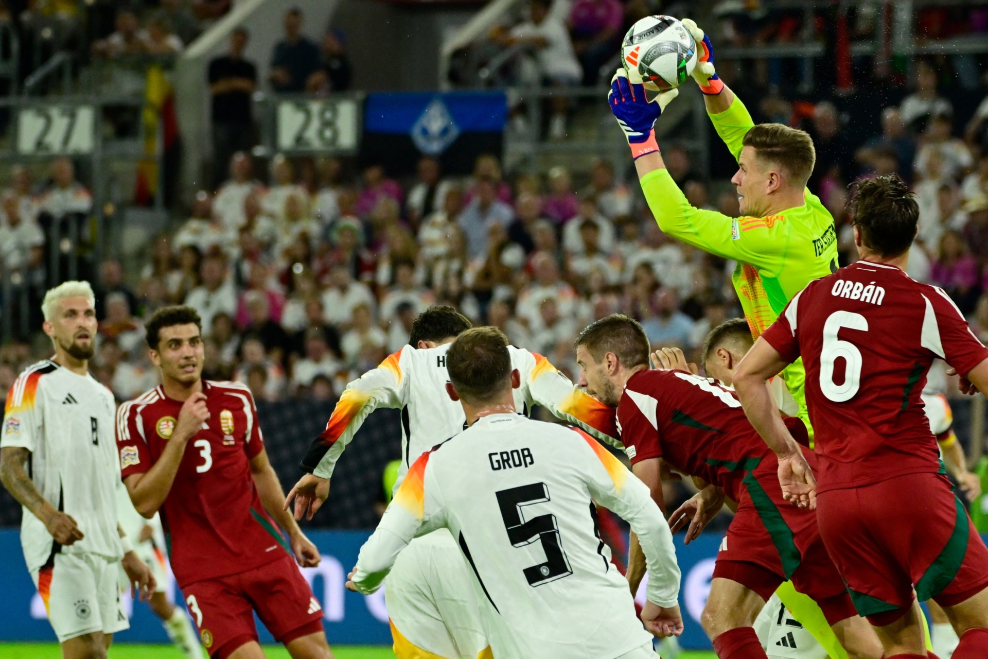 [{"clang_id":1,"value":"Fußballspiel: Torwart springt hoch, um Ball zu fangen. Spieler in weißen und roten Trikots um ihn herum. Zuschauer im Hintergrund."}]