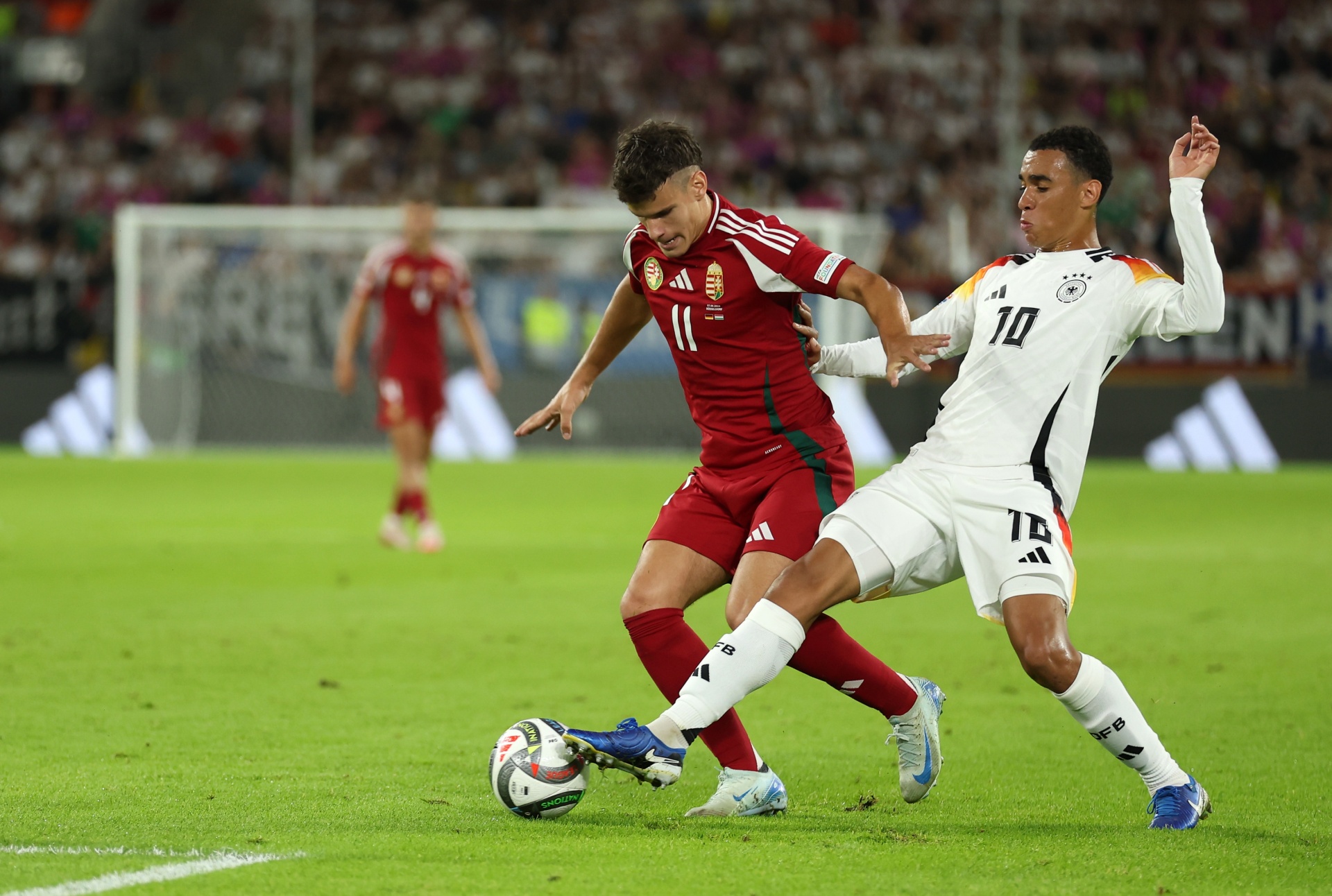 [{"clang_id":1,"value":"Fußballspiel: Spieler in roten und weißen Trikots kämpfen um den Ball auf grünem Rasen. Im Hintergrund Zuschauer."}]