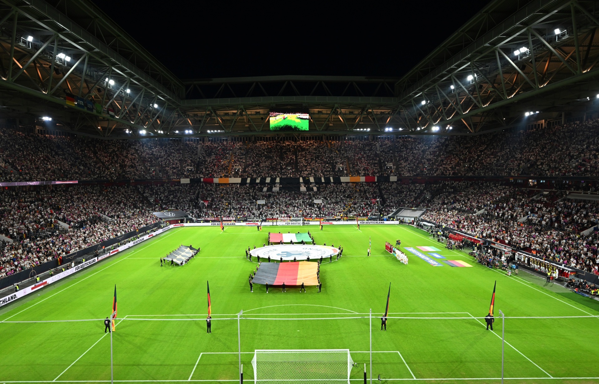 [{"clang_id":1,"value":"Fußballstadion bei Nacht, volles Publikum. Auf dem Rasen Vorbereitungen für ein Spiel mit Fahnen (Deutschland, Niederlande) und Personen in Uniform."}]