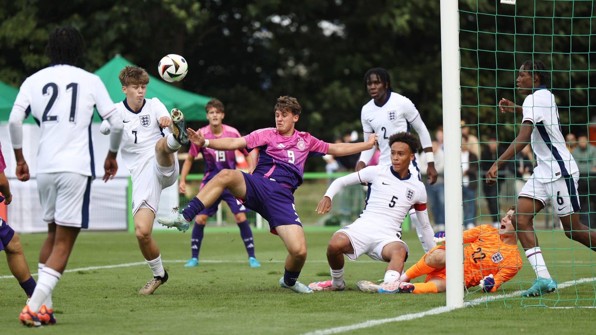 [{"clang_id":1,"value":"Fußballspiel: Spieler in weißen und violetten Trikots kämpfen um den Ball vor dem Tor. Der Ball ist in der Luft, der Torwart bereitet sich auf die Abwehr vor."}]