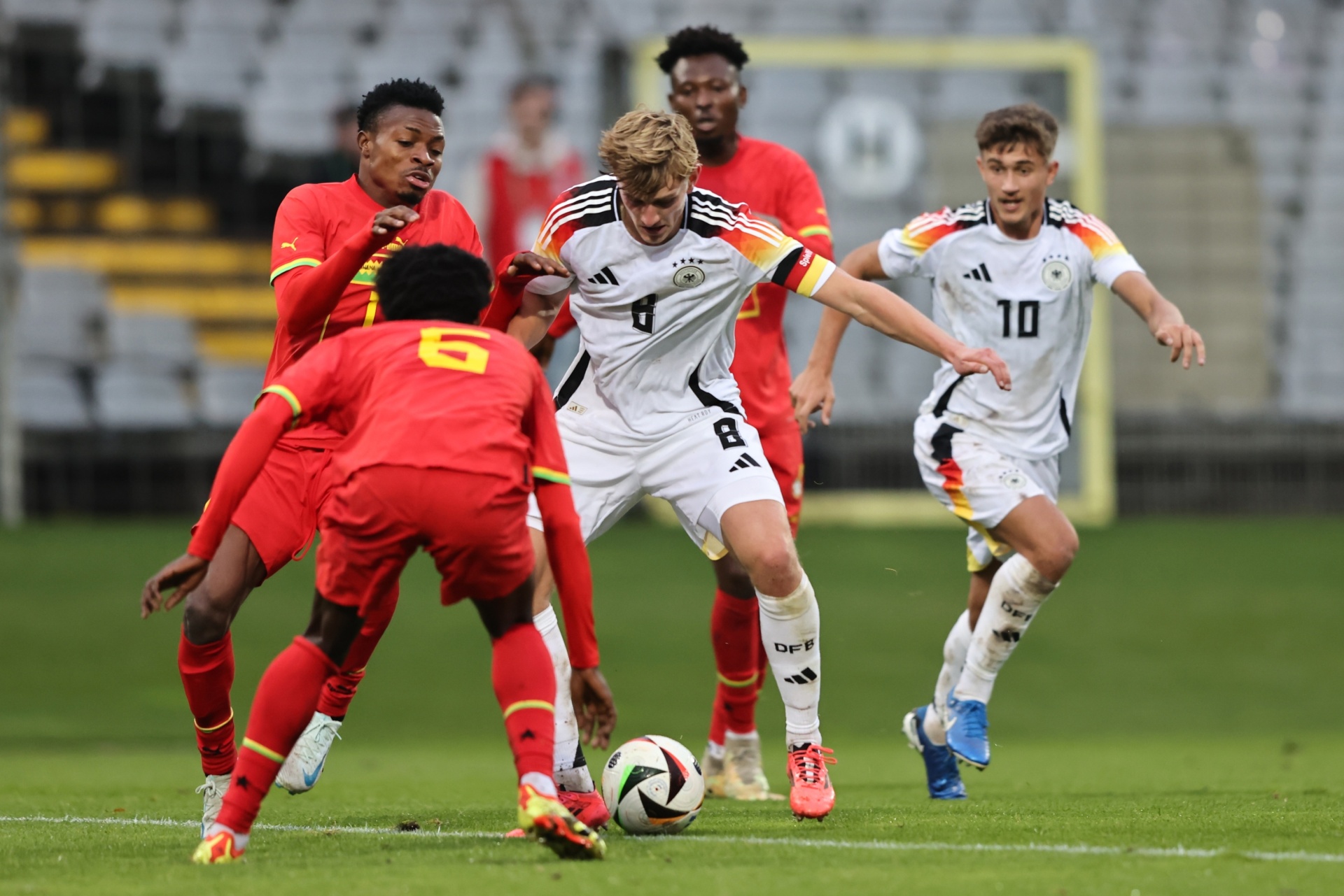 [{"clang_id":1,"value":"Fußballspiel. Zwei Spieler mit weißen Trikots kämpfen um den Ball gegen drei Spieler mit roten Trikots auf grünem Rasen. Im Hintergrund Zuschauerreihen."}]