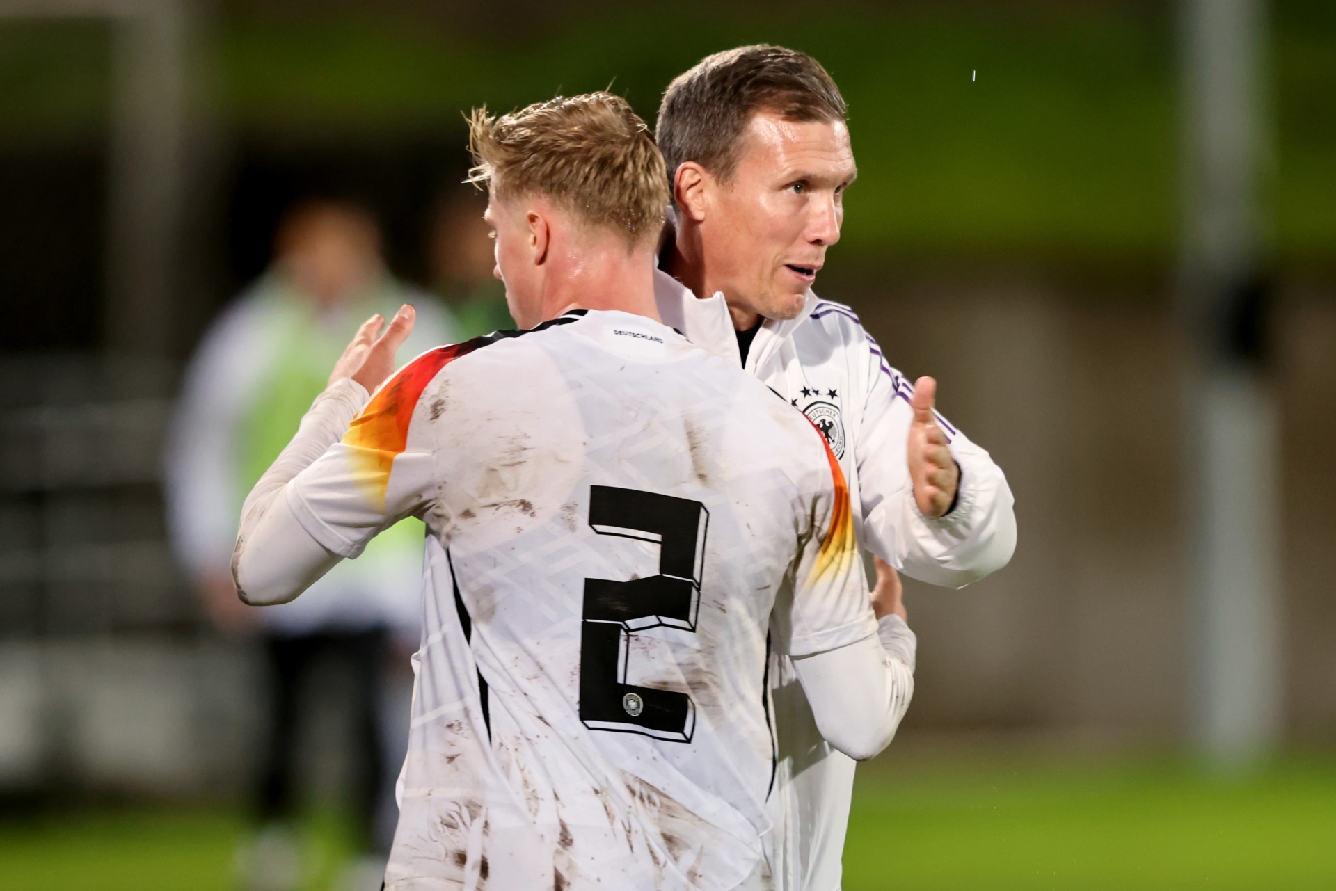 [{"clang_id":1,"value":"Zwei Fußballspieler in weißen Trikots der deutschen Nationalmannschaft feiern mit gestreckten Armen. Auf dem Rücken des einen Spielers ist die Zahl 2 zu sehen. Hintergrund: Fußballfeld."}]