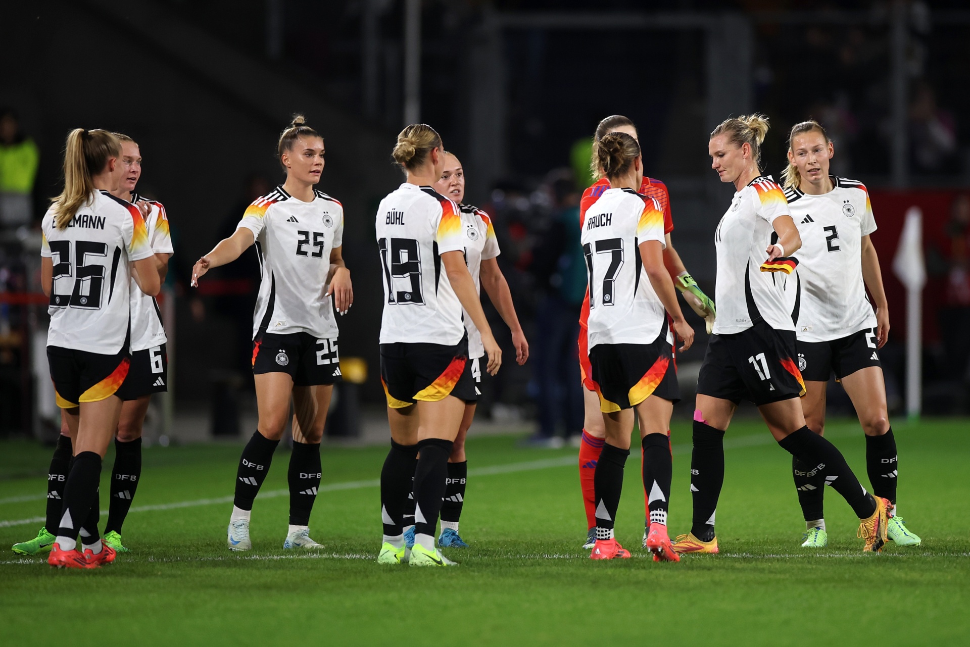 [{"clang_id":1,"value":"Frauenfußballteam in weißen Trikots mit schwarzen und roten Akzenten steht auf grünem Rasen, einige mit hochgebundenen Haaren, während eines Spiels."}]