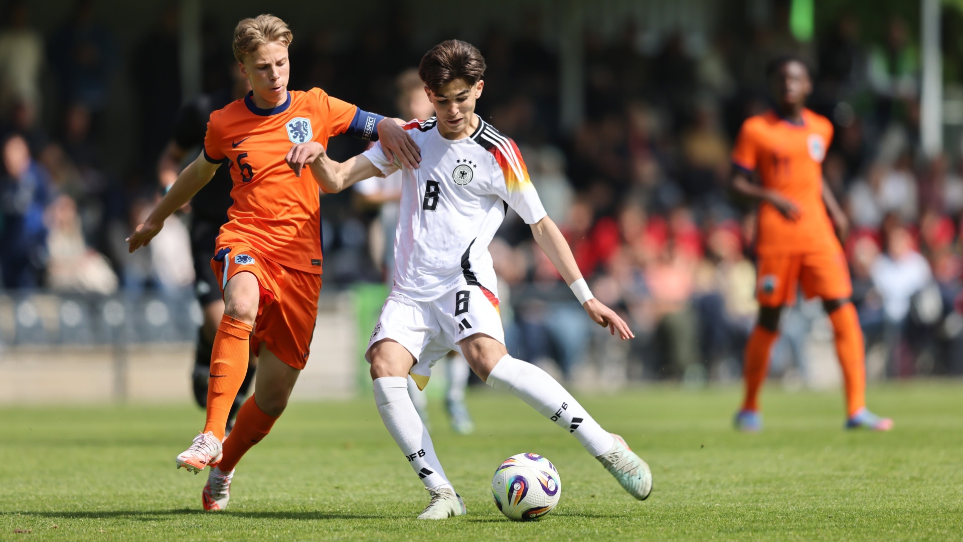 [{"clang_id":1,"value":"Zwei Fußballspieler im Spiel. Links: Spieler mit orangefarbenem Trikot. Rechts: Spieler mit weiß-schwarzem Trikot, der den Ball spielt. Rasen im Hintergrund."}]