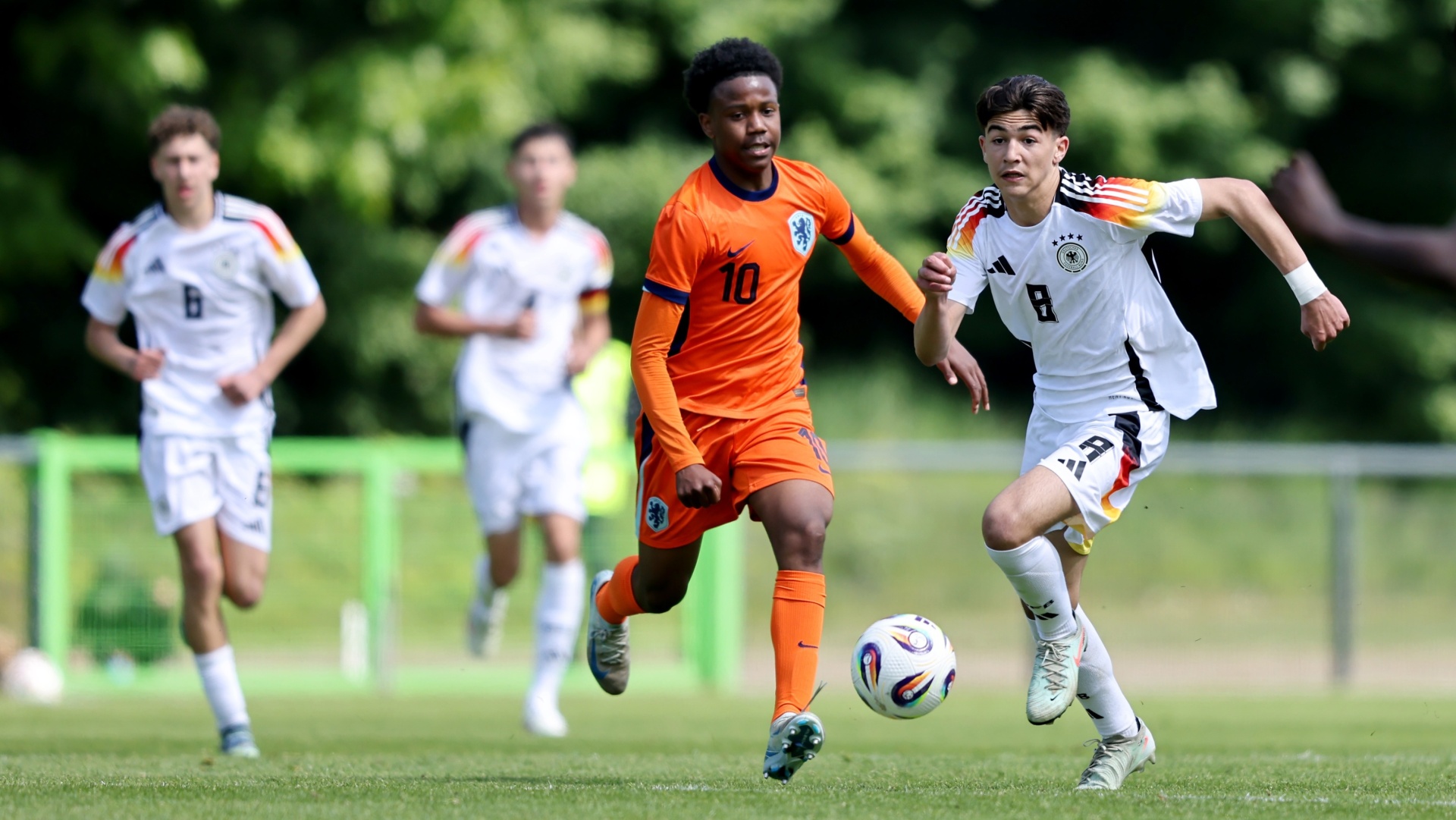[{"clang_id":1,"value":"Fußballspiel: Zwei Spieler dribbeln den Ball auf einem grünen Rasenfeld. Links und im Hintergrund weitere Spieler in unterschiedlichen Trikots."}]