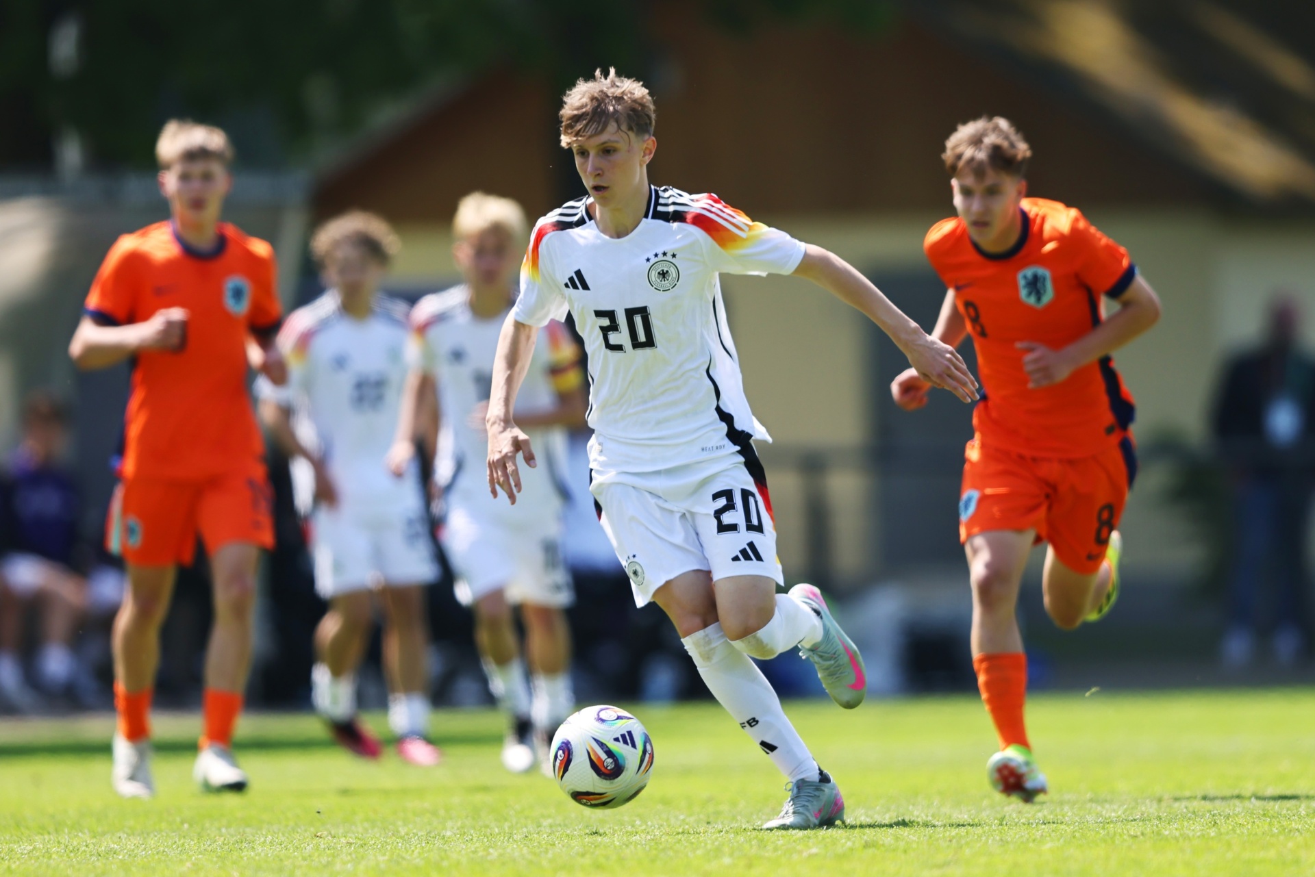 [{"clang_id":1,"value":"Jugendfußballspiel. Spieler mit Trikotnummer 20 dribbelt am Ball, umgeben von Spielern in orangefarbenen und weißen Trikots auf grünem Rasen."}]