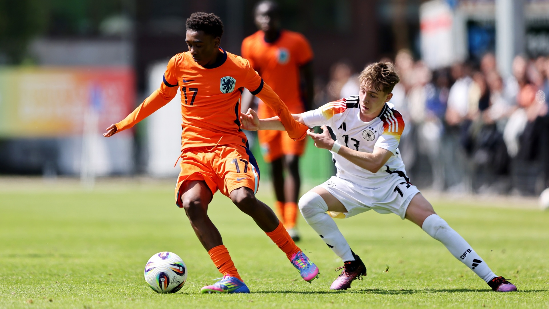 [{"clang_id":1,"value":"Zwei Fußballspieler im Wettkampf. Links in orange, rechts in schwarz-weiß, kämpfen um den Ball auf Grün. Zuschauer im Hintergrund."}]