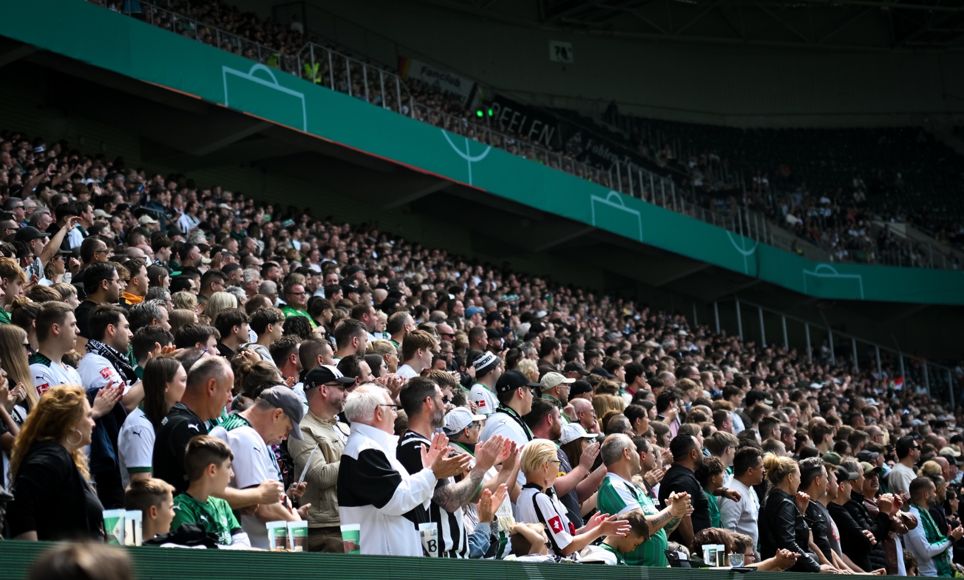 [{"clang_id":1,"value":"Volles Fußballstadion. Menschen sitzen dicht gedrängt auf den Tribünen und klatschen. Überwiegend schwarz-weiße Kleidung im Publikum."}]