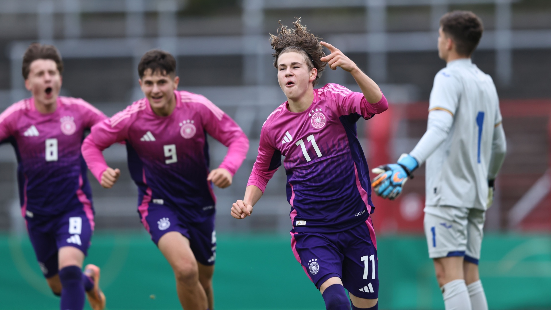 [{"clang_id":1,"value":"Fußballspieler in pinken Trikots jubeln nach einem Tor. Ein Spieler mit Nummer 11 zeigt mit dem Finger nach oben. Im Hintergrund der Torwart und weitere Spieler."}]