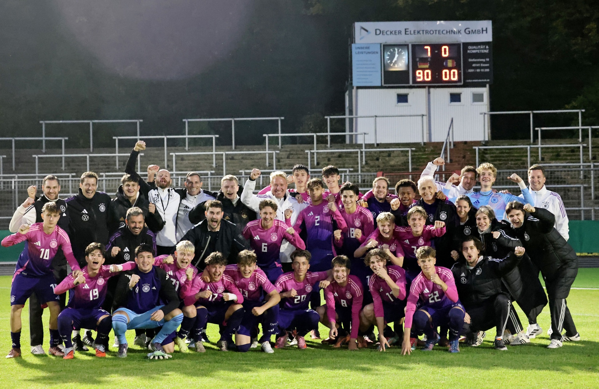 [{"clang_id":1,"value":"Fußballmannschaft in violetten und schwarzen Trikots feiert Sieg auf dem Rasen. Im Hintergrund eine Anzeigetafel mit Endergebnis 1:0 und jubelnde Personen."}]