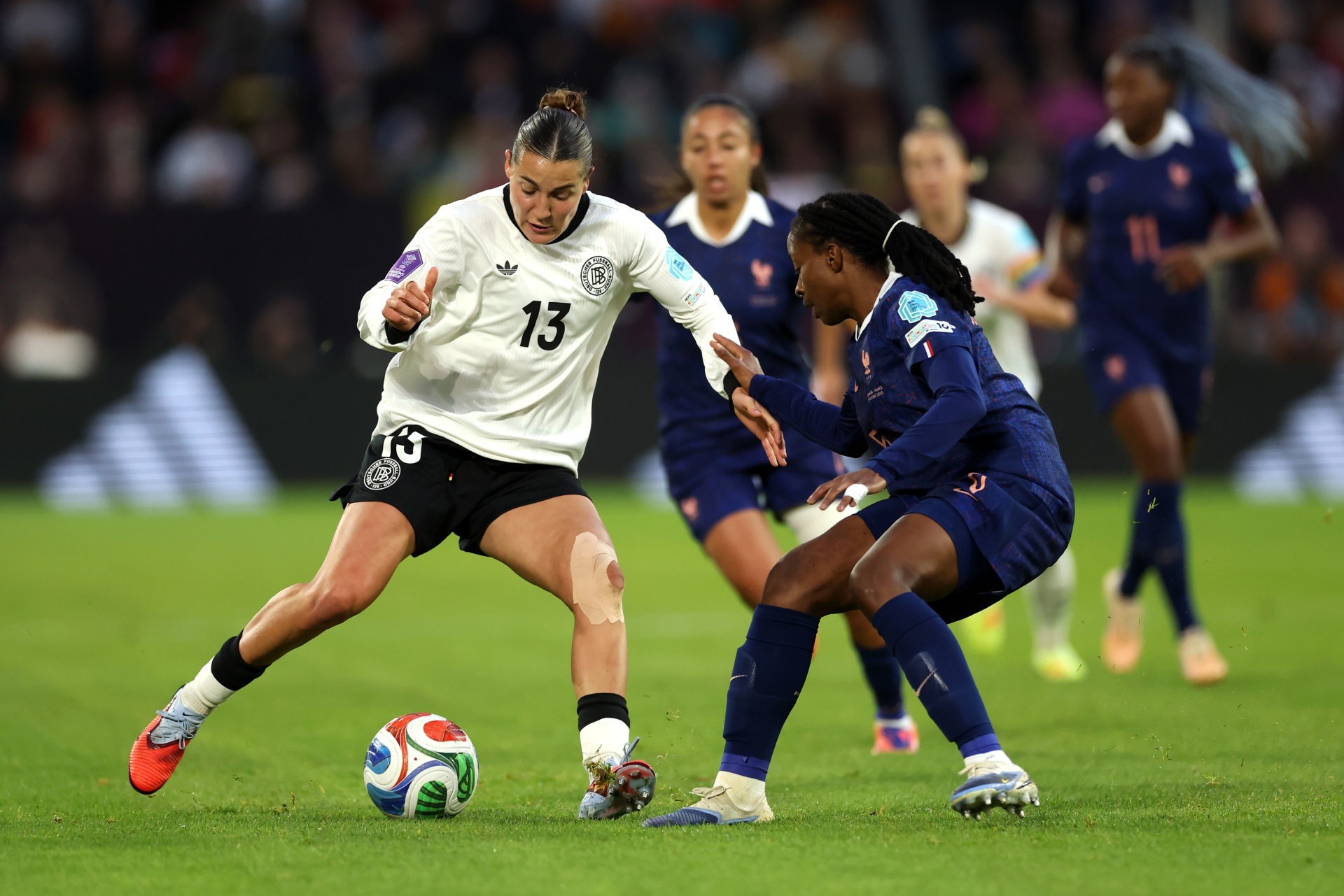 [{"clang_id":1,"value":"Zwei Fußballspielerinnen im Wettkampf. Eine Spielerin mit Nummer 13 in weißen Trikots dribbelt den Ball. Eine Gegenspielerin in blau versucht, den Ball zu erobern. Rasen im Hintergrund."}]