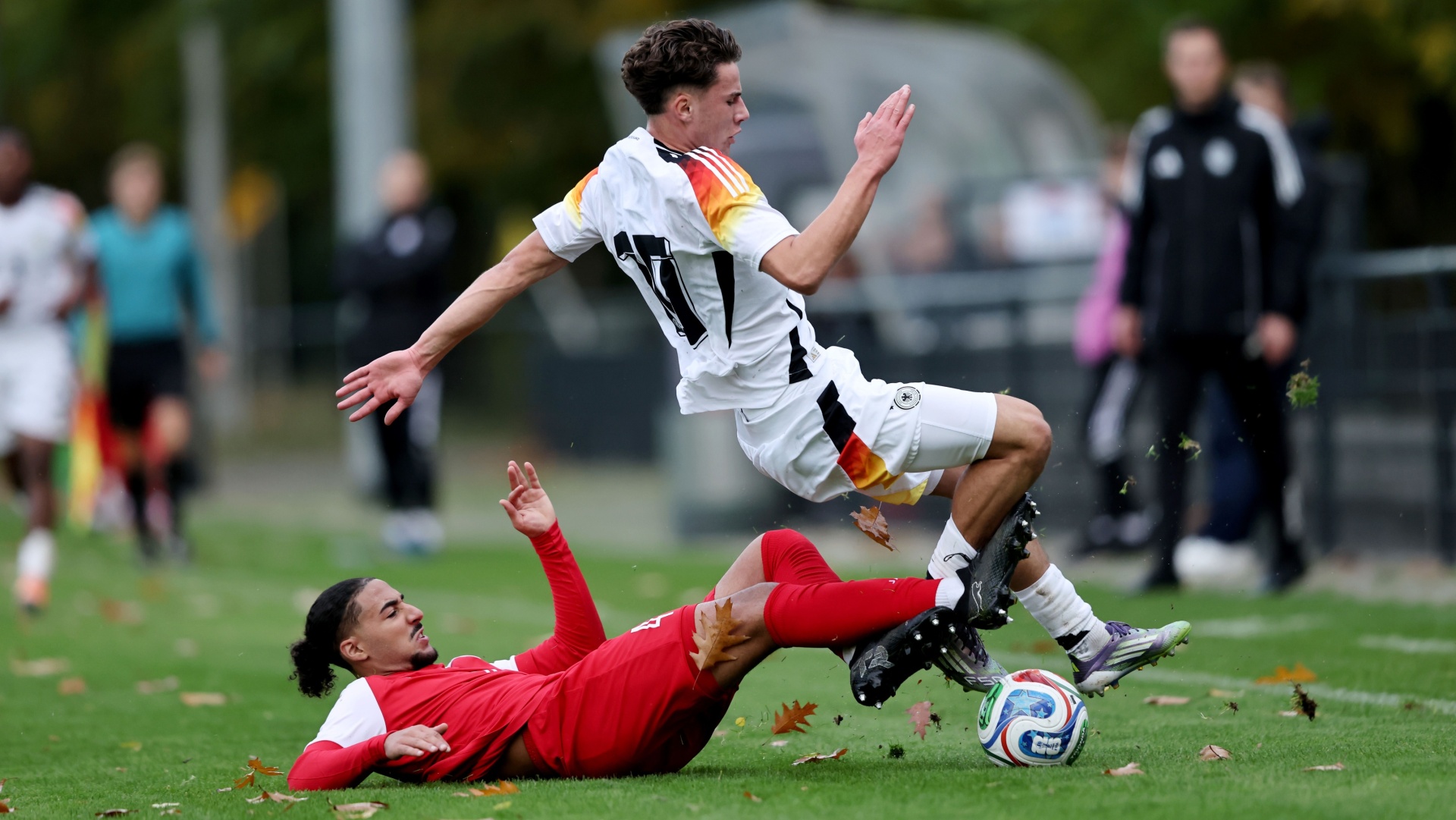 [{"clang_id":1,"value":"Zwei Fußballspieler in Aktion. Ein Spieler in Weiß-Schwarz rutscht über einen in Rot gekleideten Spieler, Ball dazwischen. Rasen und Zuschauer im Hintergrund."}]