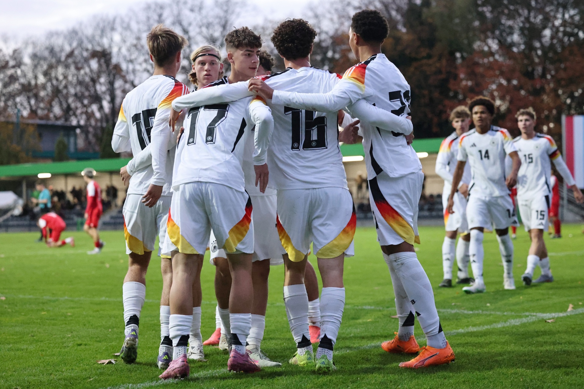 [{"clang_id":1,"value":"Fußballspieler im weißen Trikot mit Deutschland-Flagge feiern auf einem grünen Rasen. Im Hintergrund weitere Spieler und Zuschauer."}]