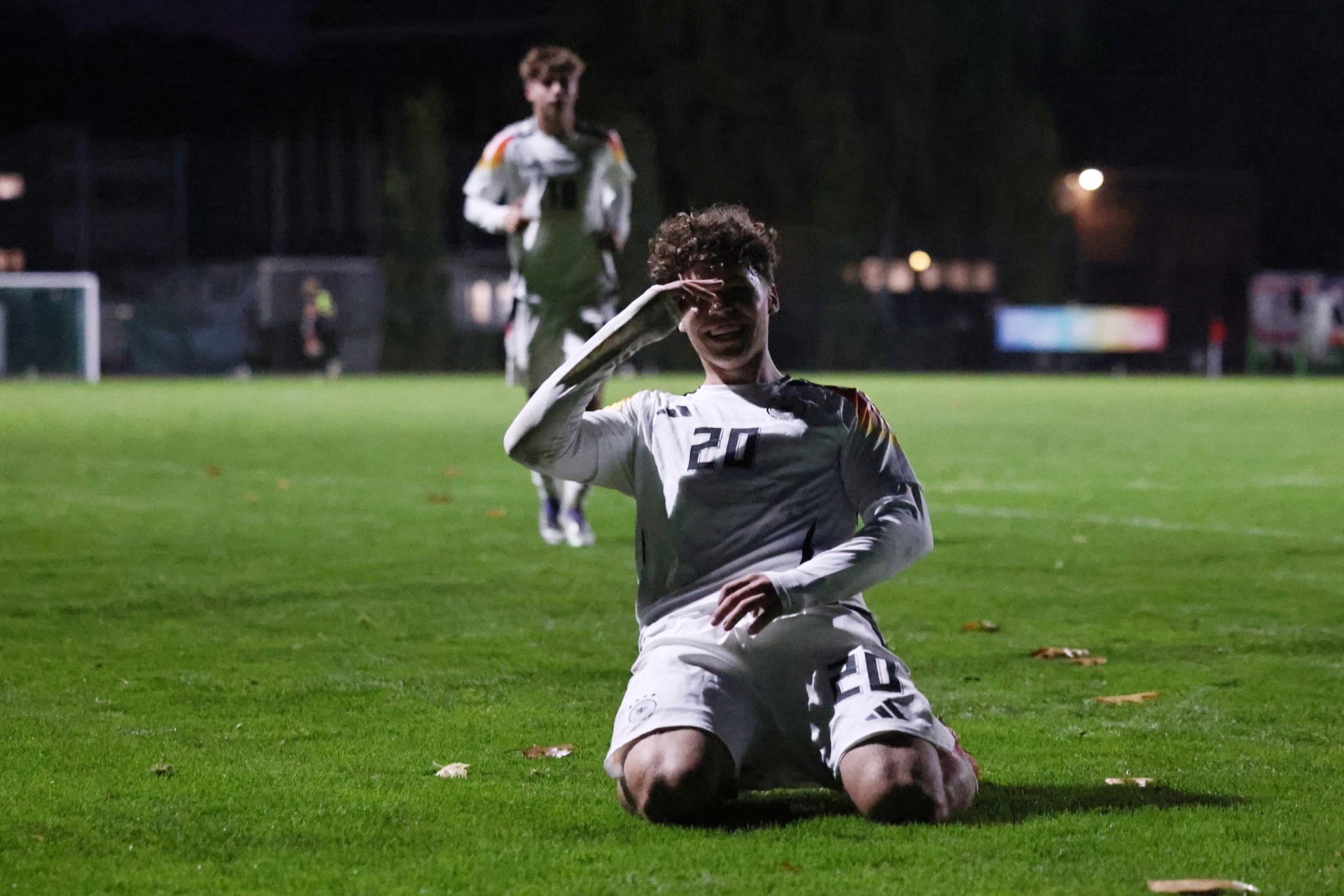 [{"clang_id":1,"value":"Fußballspieler kniet auf grünem Rasen, jubelt mit erhobener Hand. Im Hintergrund ein weiterer Spieler und Stadionbeleuchtung. Dunkel."}]