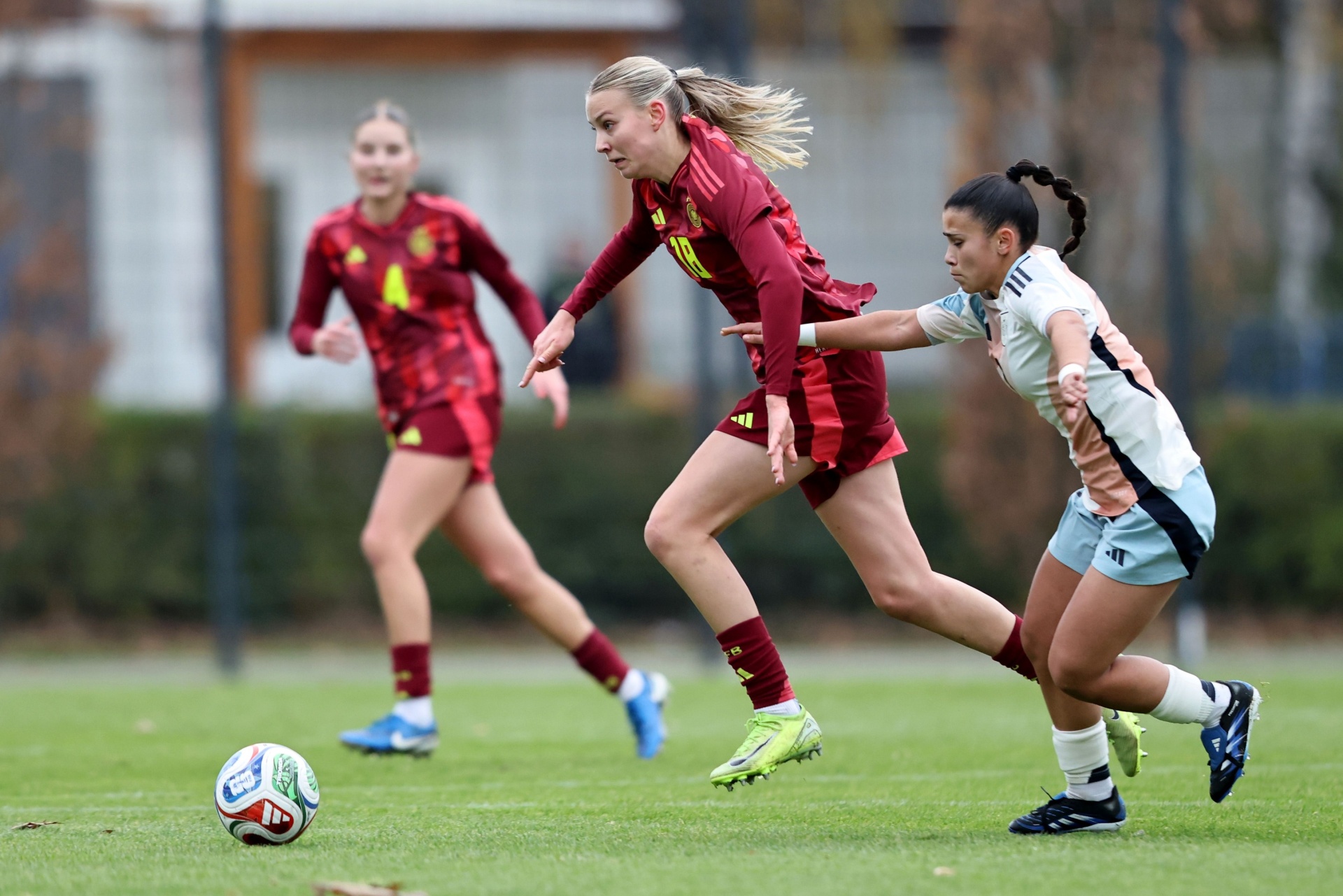 [{"clang_id":1,"value":"Drei Fußballspielerinnen auf Grün: Eine in maroon und eine in hellblau kämpfen um den Ball. Im Hintergrund eine weitere Spielerin in maroon."}]