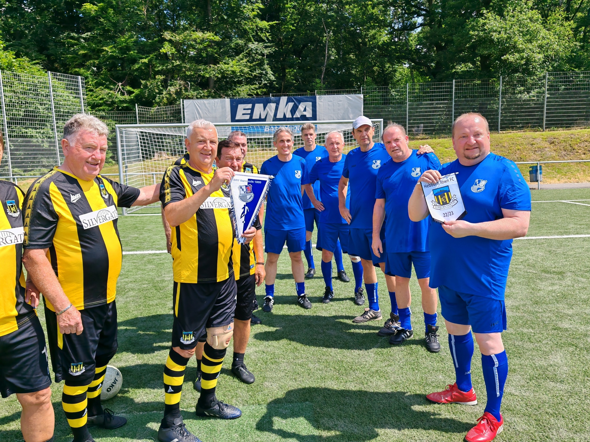 [{"clang_id":1,"value":"Fußballmannschaft in Vereinskleidung steht auf einem grünen Rasen vor einem Fußballtor. Einige halten Urkunden oder Ausweise."}]