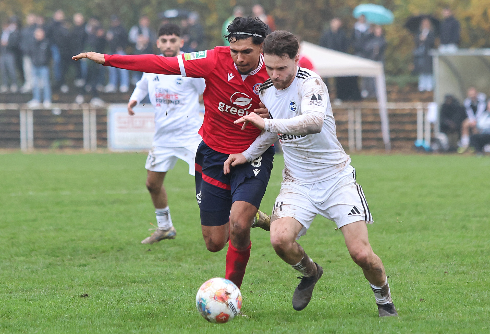 [{"clang_id":1,"value":"Fußballspiel: Zwei Spieler kämpfen um den Ball. Ein Spieler in rotem Trikot und Shorts, der andere in weißem Trikot und Shorts. Zuschauer im Hintergrund."}]