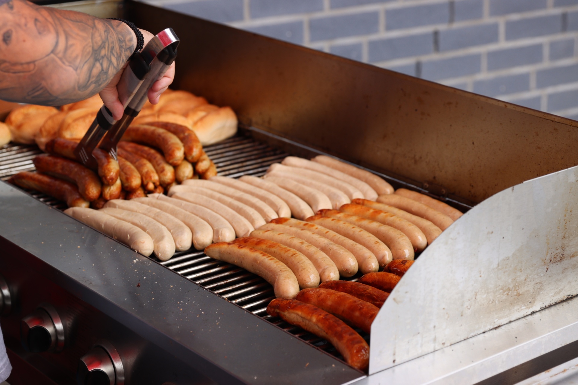 [{"clang_id":1,"value":"Grill mit vielen rohen Würsten in verschiedenen Sorten. Eine Person mit tätowierten Armen greift mit einer Zange nach einer Wurst. Hintergrund: blaue Kacheln."}]