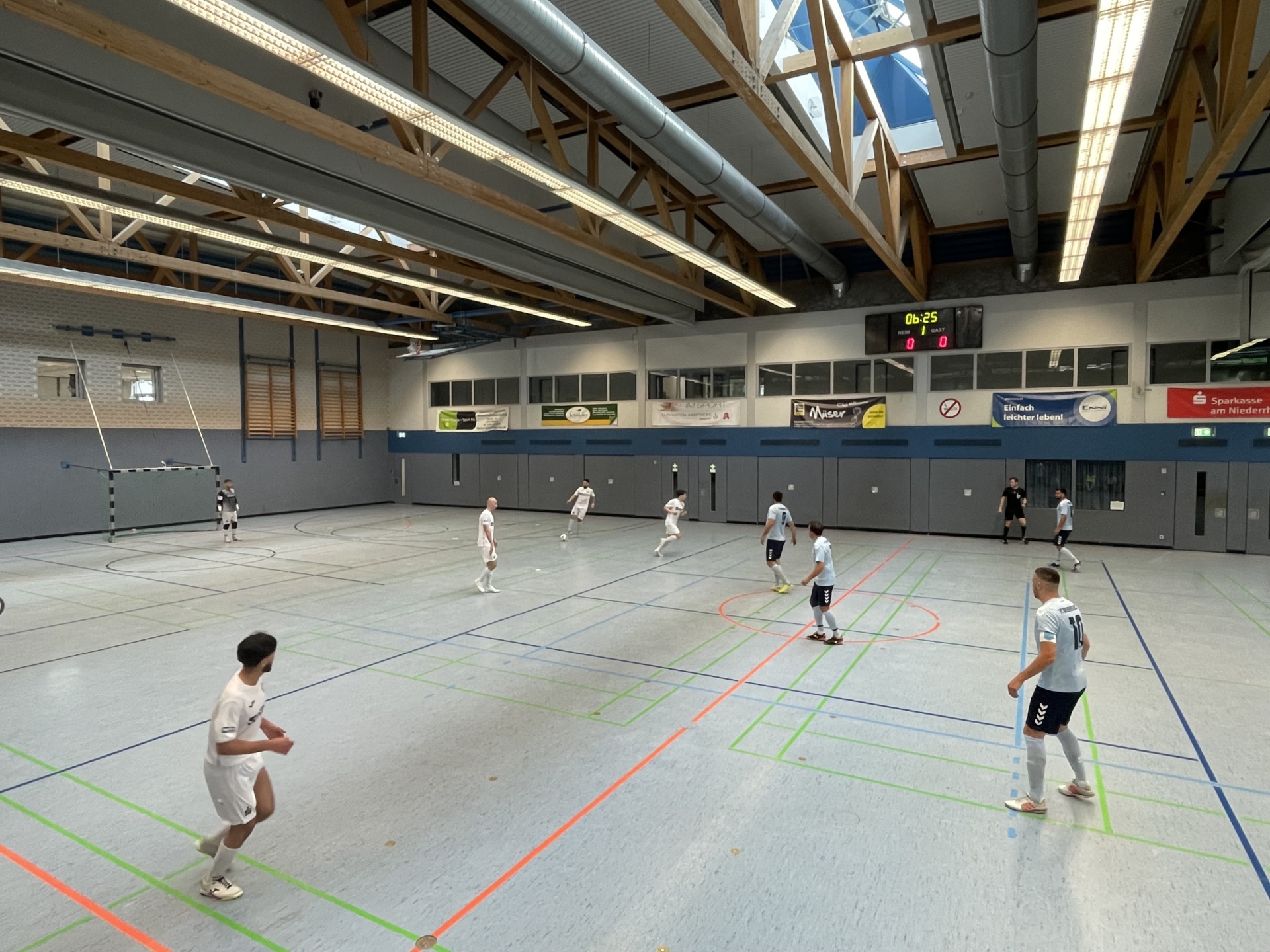 [{"clang_id":1,"value":"Sporthalle mit Handballspiel. Mehrere Spieler in weißen und dunklen Trikots auf einem farbig markierten Spielfeld. Zeitanzeige: 06:25, Stand: 0-0."}]