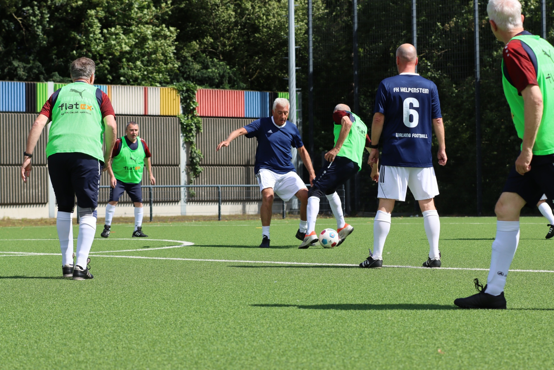 [{"clang_id":1,"value":"Fußballspiel älterer Herren auf Rasenplatz. Ein Spieler schießt auf das Tor, andere Spieler stehen in der Nähe. Im Hintergrund bunte Gebäude und Bäume."}]