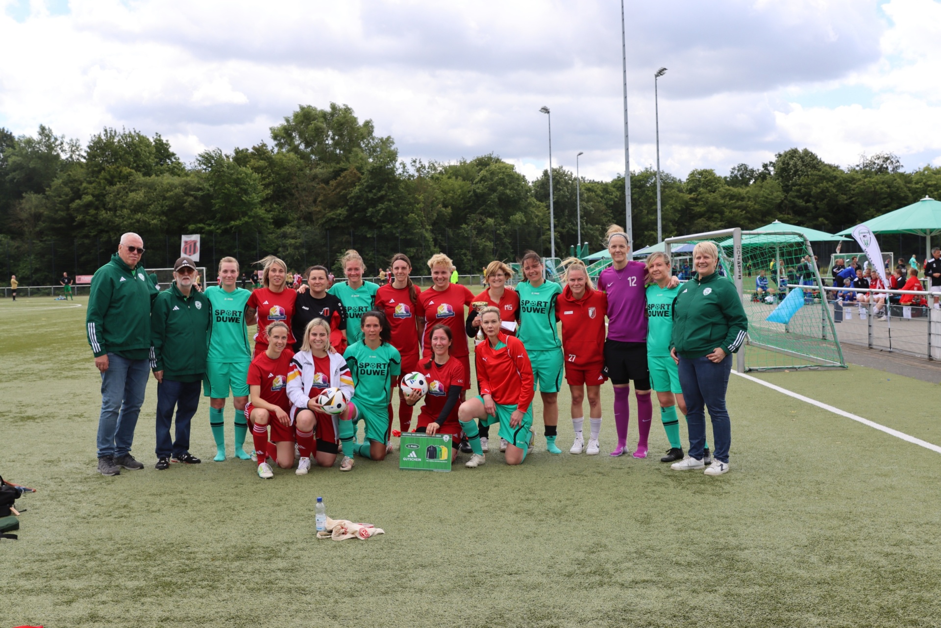 [{"clang_id":1,"value":"Fußballmannschaften in grünen und roten Trikots stehen auf einem grünen Kunstrasenplatz vor dem Spiel. Trainer in grünen Jacken stehen an den Seiten. Im Hintergrund Bäume und ein Fußballtor."}]