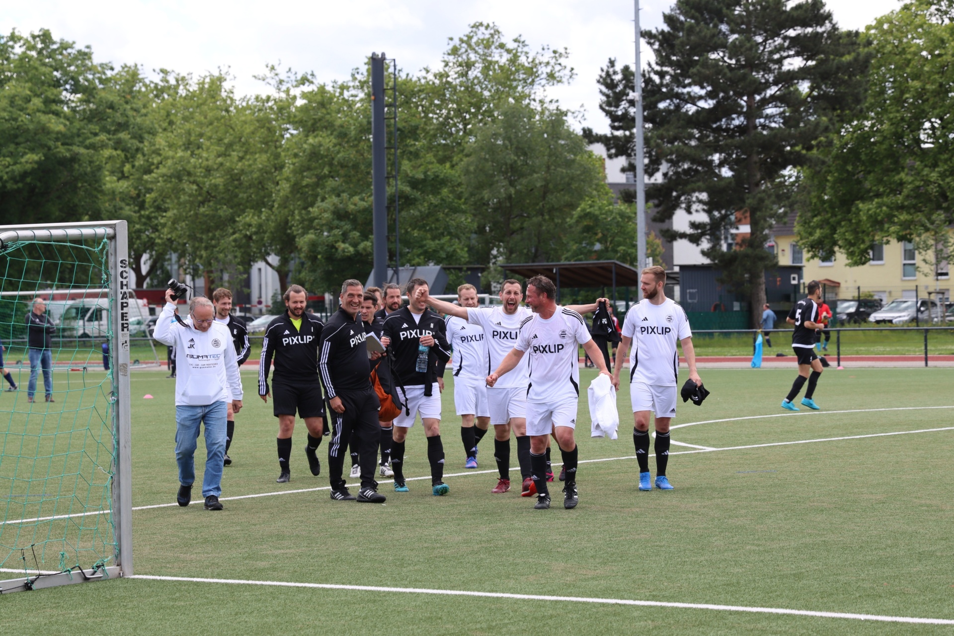 [{"clang_id":1,"value":"Fußballmannschaft in schwarzen und weißen Trikots mit Schriftzug \"PIXLIP\" auf dem Platz. Im Hintergrund Bäume und Gebäude."}]