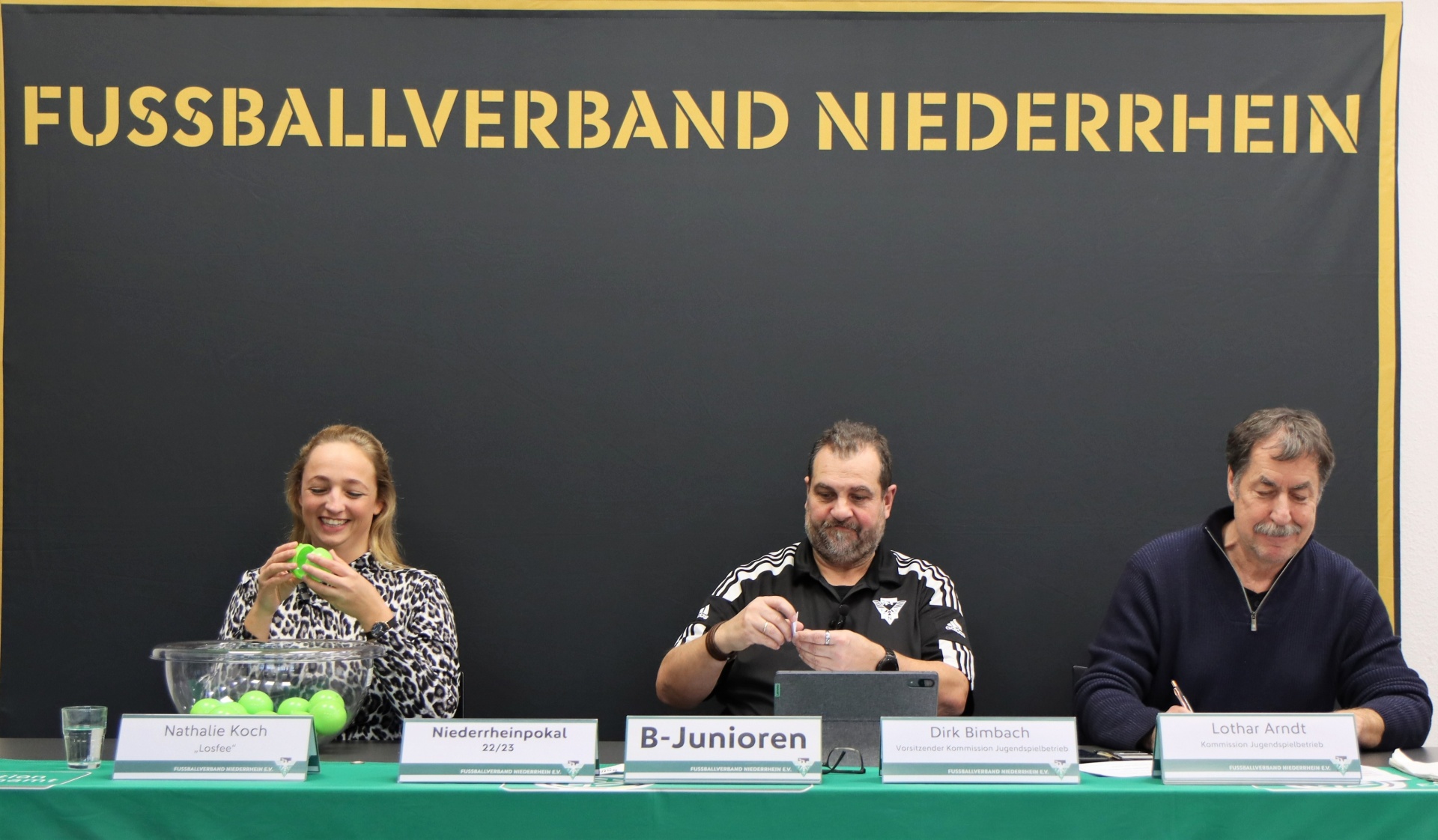 [{"clang_id":1,"value":"Drei Personen sitzen an einem Tisch mit Namensschildern vor einem Banner mit dem Schriftzug \"FUSSBALLVERBAND NIEDERRHEIN\". Von links: Nathalie Koch, Dirk Bimbach, Lothar Arndt."}]
