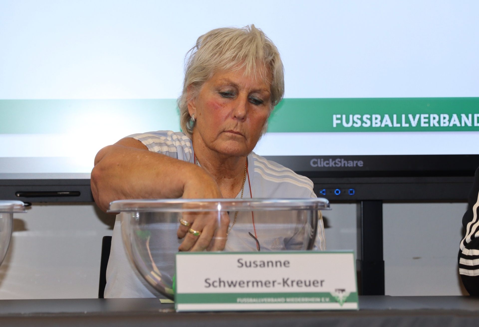 [{"clang_id":1,"value":"Frau mit blonden, kurzen Haaren spricht ans Publikum. Vor ihr Namensschild mit \"Susanne Schwermer-Kreuer\". Im Hintergrund eine Wand mit Schriftzug \"FUSSBALLVERBAND\"."}]