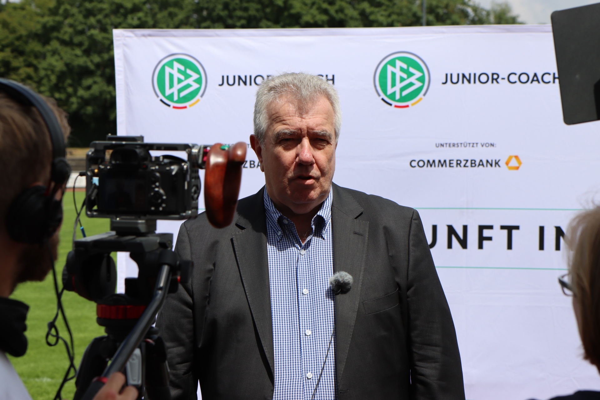 [{"clang_id":1,"value":"Mann mit Jackett vor Werbebanner. Kameraleute und Mikrofone im Vordergrund, Rasen im Hintergrund."}]