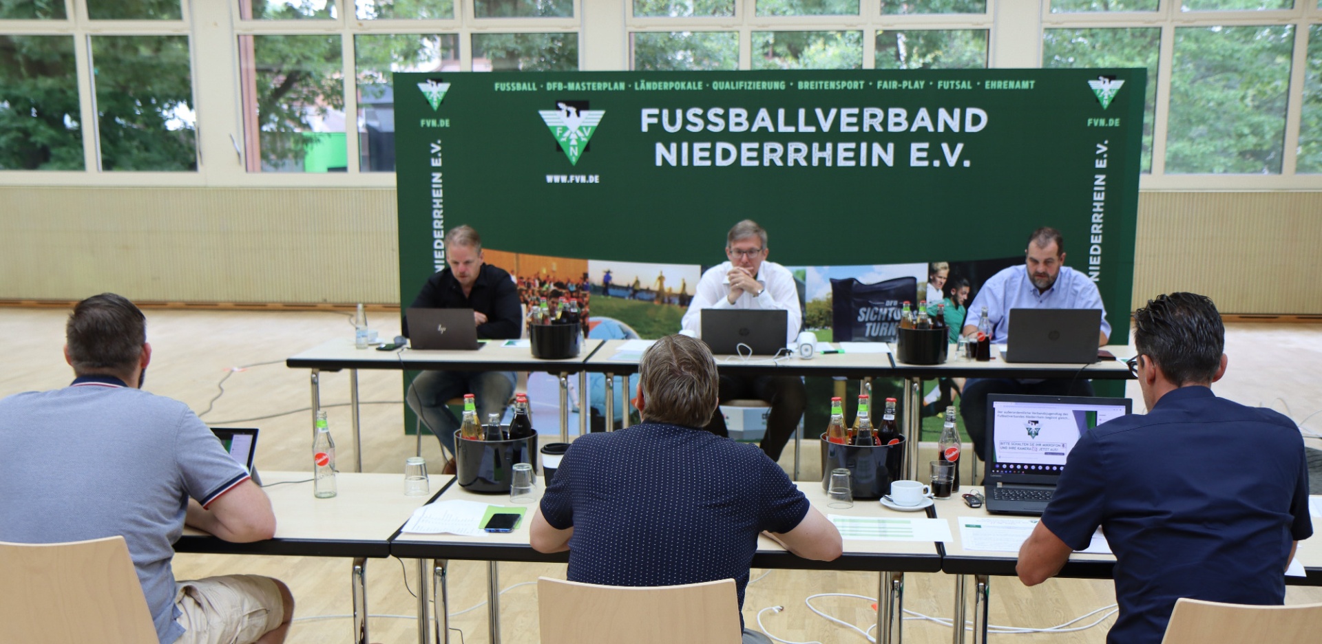 [{"clang_id":1,"value":"Konferenzraum mit Tisch, an dem mehrere Personen sitzen und auf Laptops arbeiten. Im Hintergrund ein Banner mit dem Schriftzug \"Fussballverband Niederrhein E.V.\"."}]