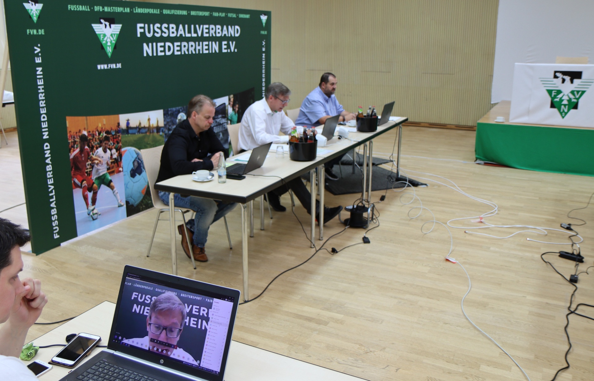 [{"clang_id":1,"value":"Konferenzraum mit Tischreihe. Vier Männer sitzen an Tischen mit Laptops und Notizen. Im Hintergrund Banner des Fussballverbands Niederrhein und eine Leinwand mit Porträt."}]