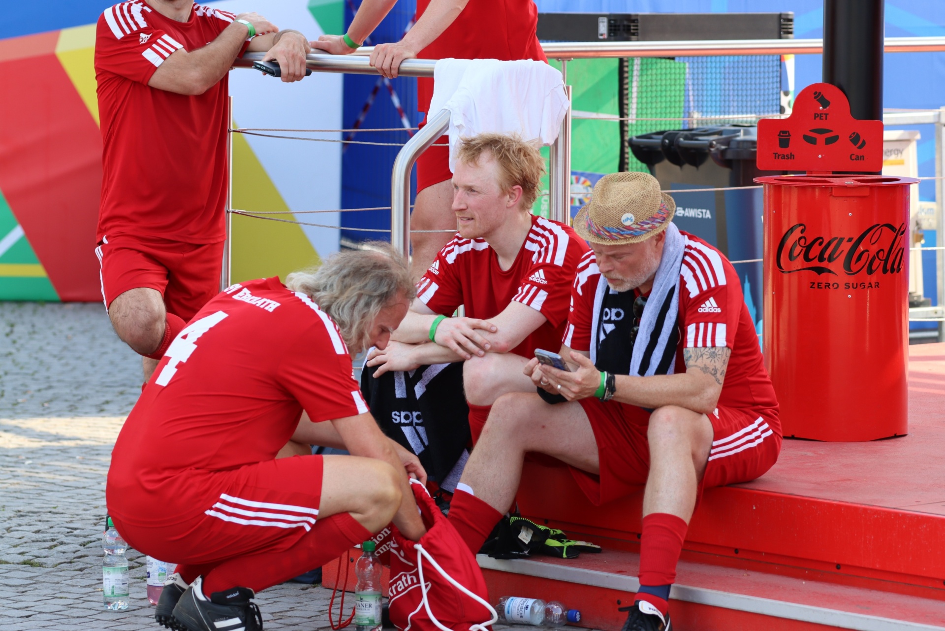 [{"clang_id":1,"value":"Beachvolleyball: Spieler in roten Trikots sitzen auf dem Sand. Ein Arzt untersucht einen Spieler am linken Bein. Im Hintergrund eine Coca-Cola-Werbung und das Spielfeld."}]