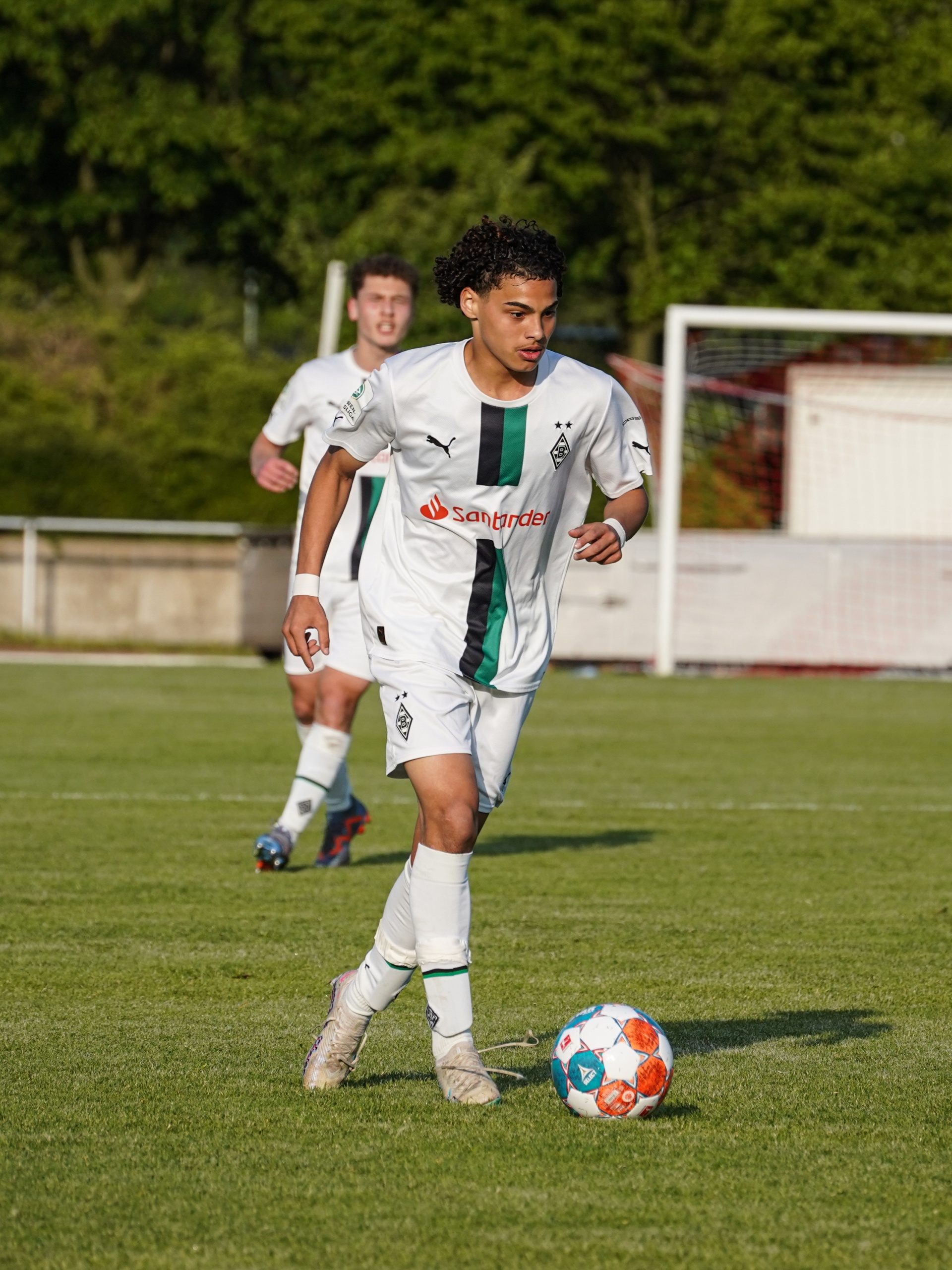 [{"clang_id":1,"value":"Zwei Fußballspieler in grünen Trikots auf einem Rasenplatz. Ein Spieler dribbelt den Ball, der andere läuft im Hintergrund."}]
