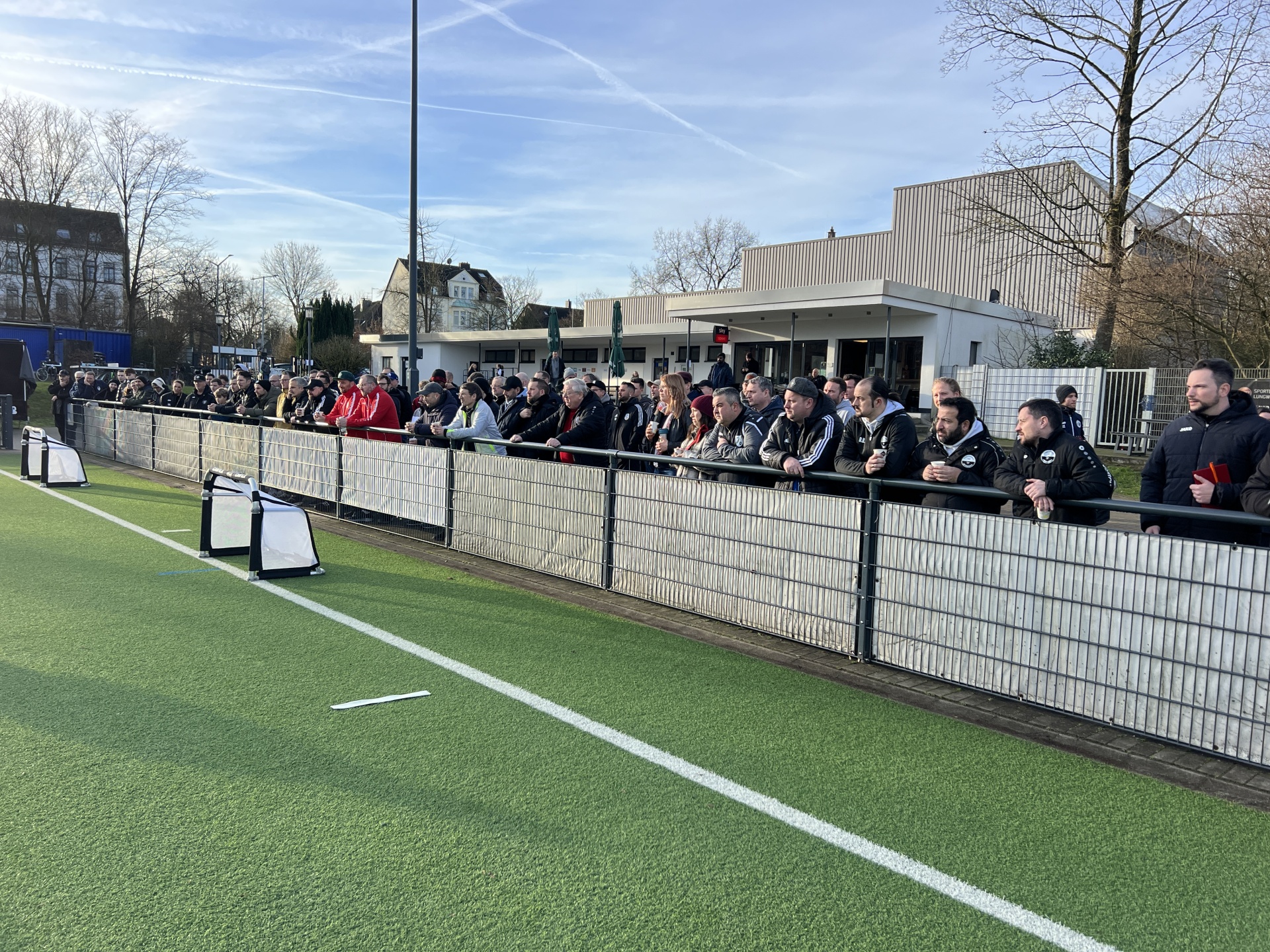 [{"clang_id":1,"value":"Fußballfeld mit Spielerbank, deren Spiegelung sich in einer Wasserfläche zeigt. Im Hintergrund Bäume und ein bewölkter Himmel."}]