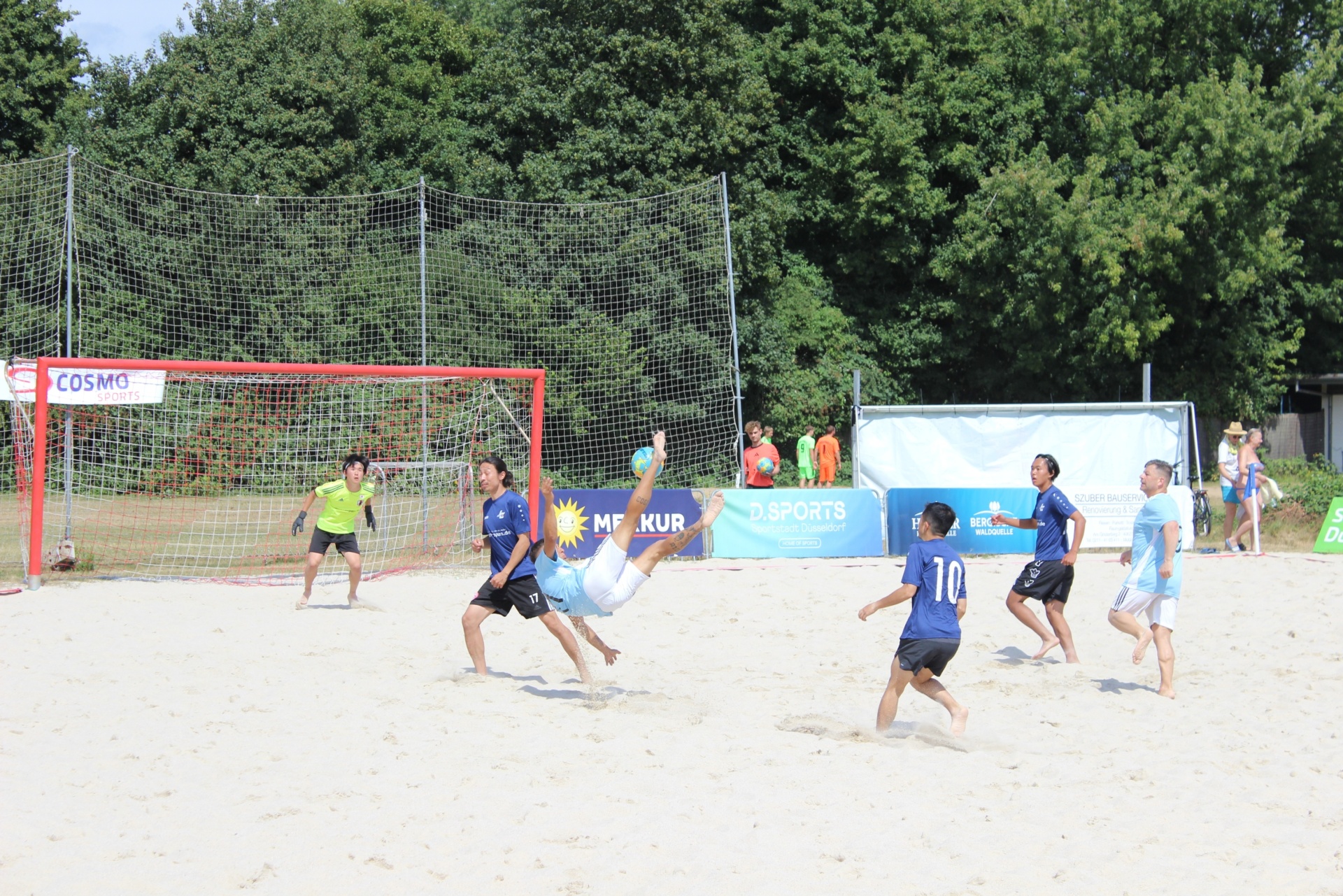 [{"clang_id":1,"value":"Beachsoccer-Spiel auf Sand. Zwei Teams mit Trikots kämpfen um den Ball vor Netzen und Zuschauern. Bäume im Hintergrund."}]