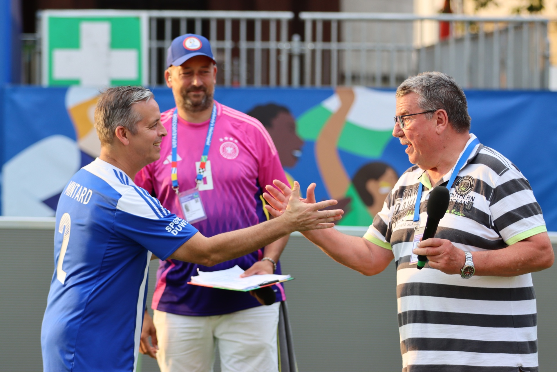 [{"clang_id":1,"value":"Zwei Männer in Sportkleidung geben sich die Hände. Im Hintergrund weitere Personen und Sportausrüstung, sowie eine blau-weiße Flagge."}]