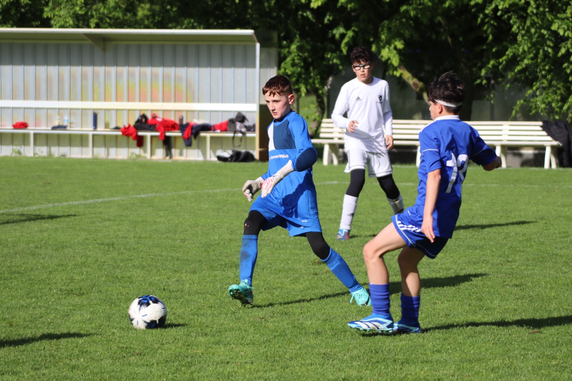 [{"clang_id":1,"value":"Drei Fussballspieler auf grünem Rasen. Links ein Spieler in blau dribbelt den Ball, dahinter ein Spieler in weiss, rechts ein weiterer in blau."}]