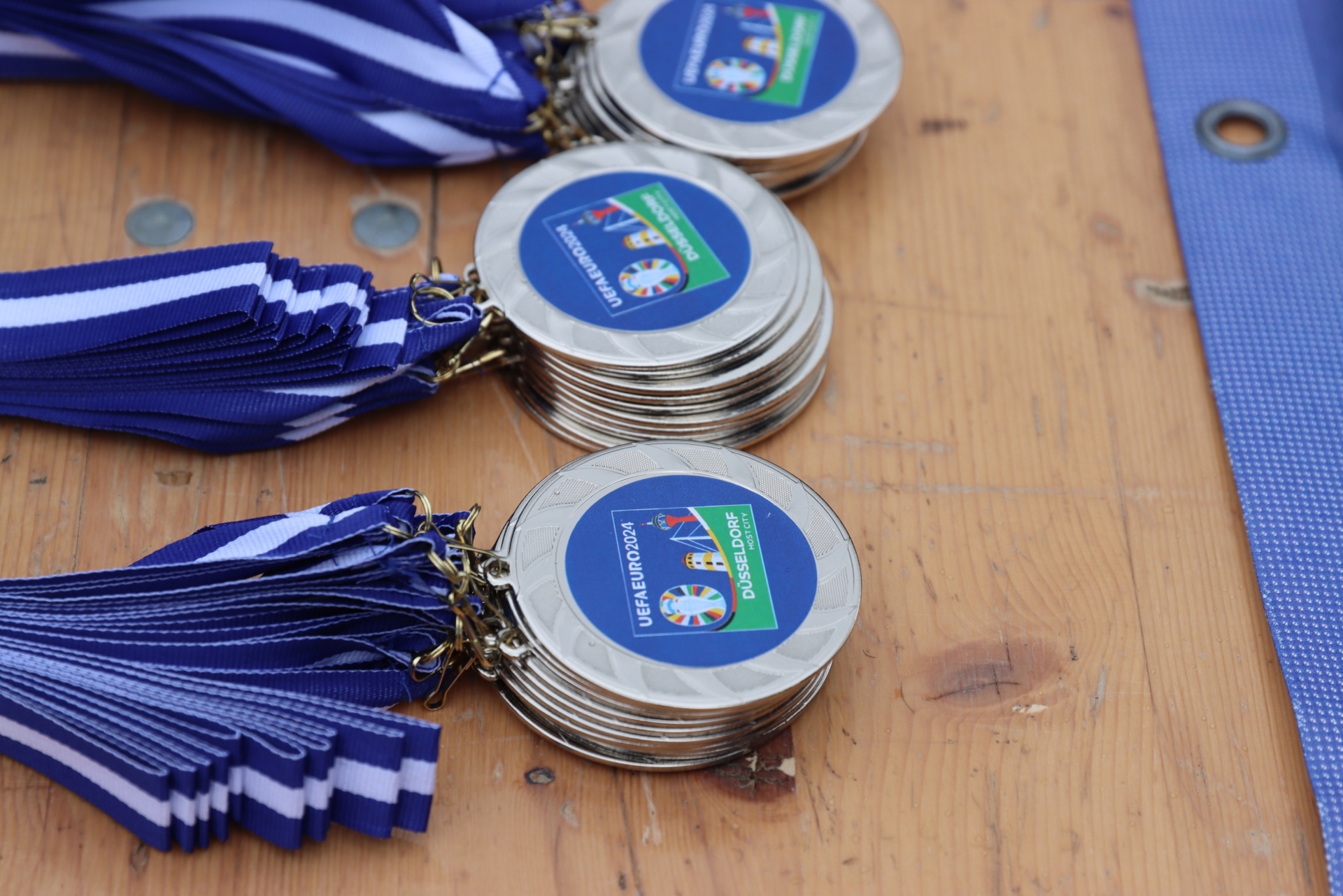 [{"clang_id":1,"value":"UEFA Euro 2024-Akreditierungen liegen auf einer hölzernen Oberfläche. Blaue Bänder und runde Anhänger mit Union Jack und Schriftzügen sind zu sehen."}]