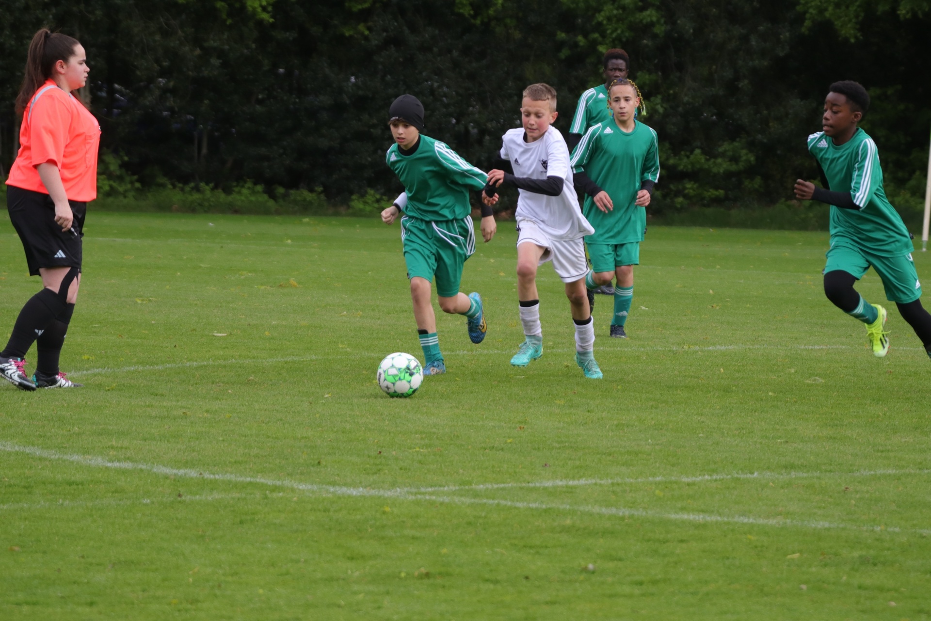 [{"clang_id":1,"value":"Fußballspiel mit Kindern: Ein Spieler in Weiß dribbelt den Ball, verfolgt von Gegenspielern in Grün. Schiedsrichterin am Spielfeldrand."}]
