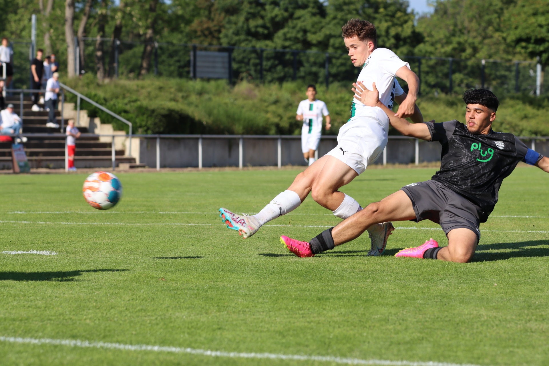[{"clang_id":1,"value":"Zwei Fußballspieler im Spiel: Ein Weiß gekleideter schießt, ein Schwarz gekleideter rutscht ihn an. Im Hintergrund weitere Spieler und Zuschauer. Rasenfläche."}]