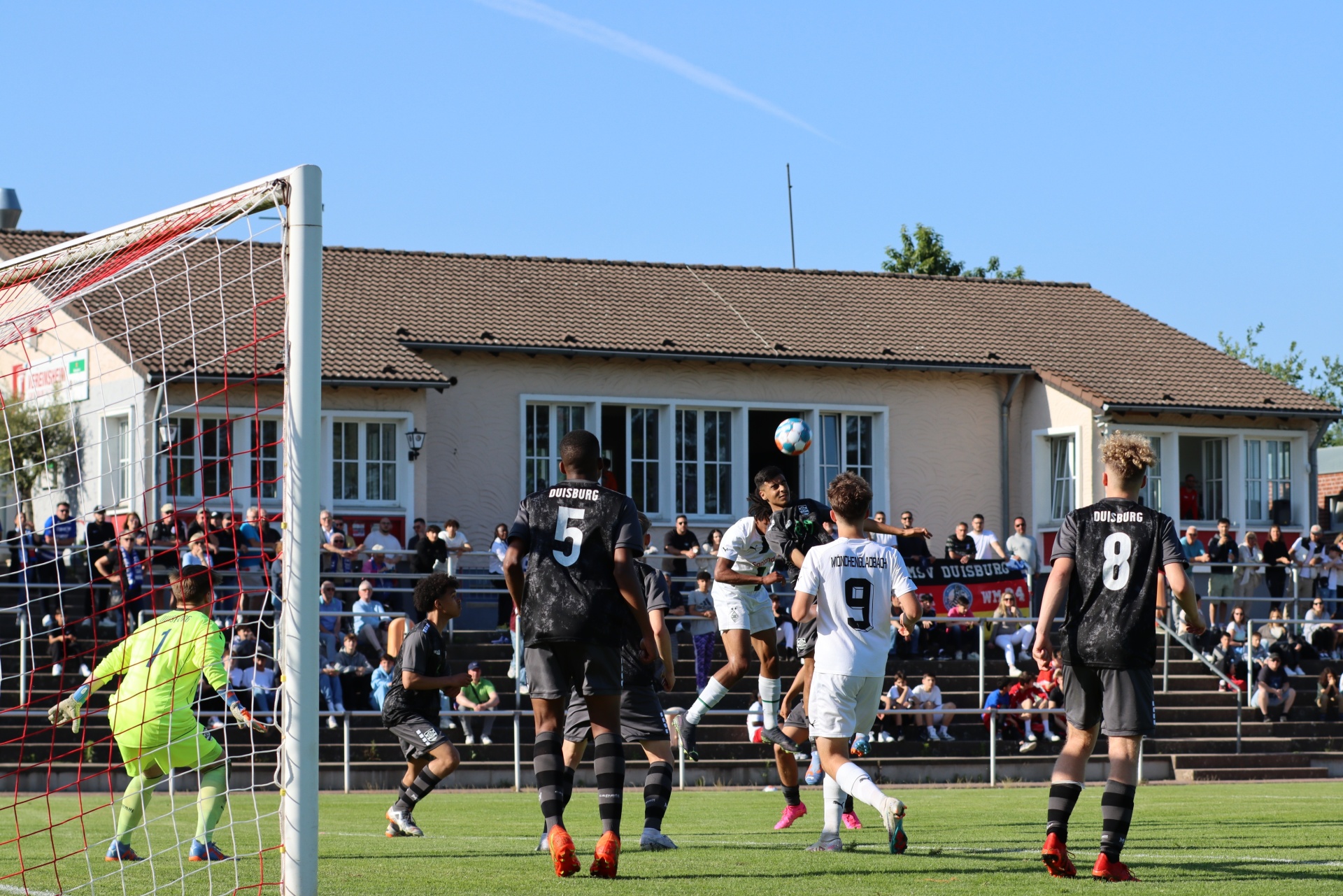 [{"clang_id":1,"value":"Fußballspiel: Spieler in schwarz und weiß kämpfen um den Ball vor dem Tor. Im Hintergrund Gebäude und Zuschauer."}]
