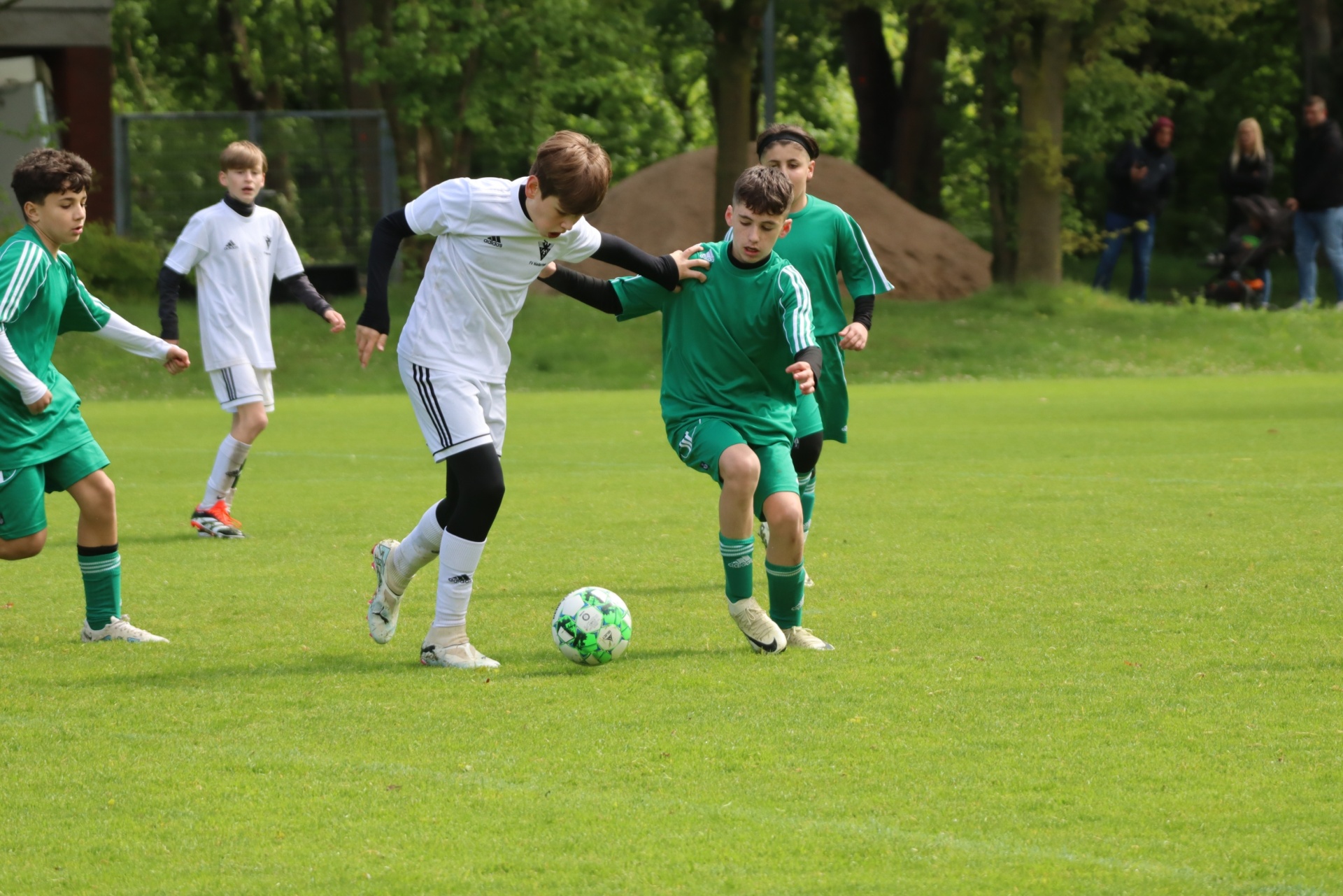 [{"clang_id":1,"value":"Jugendfußballspiel auf grünem Rasen. Zwei Spieler im Zweikampf um den Ball, weitere Spieler im Hintergrund."}]