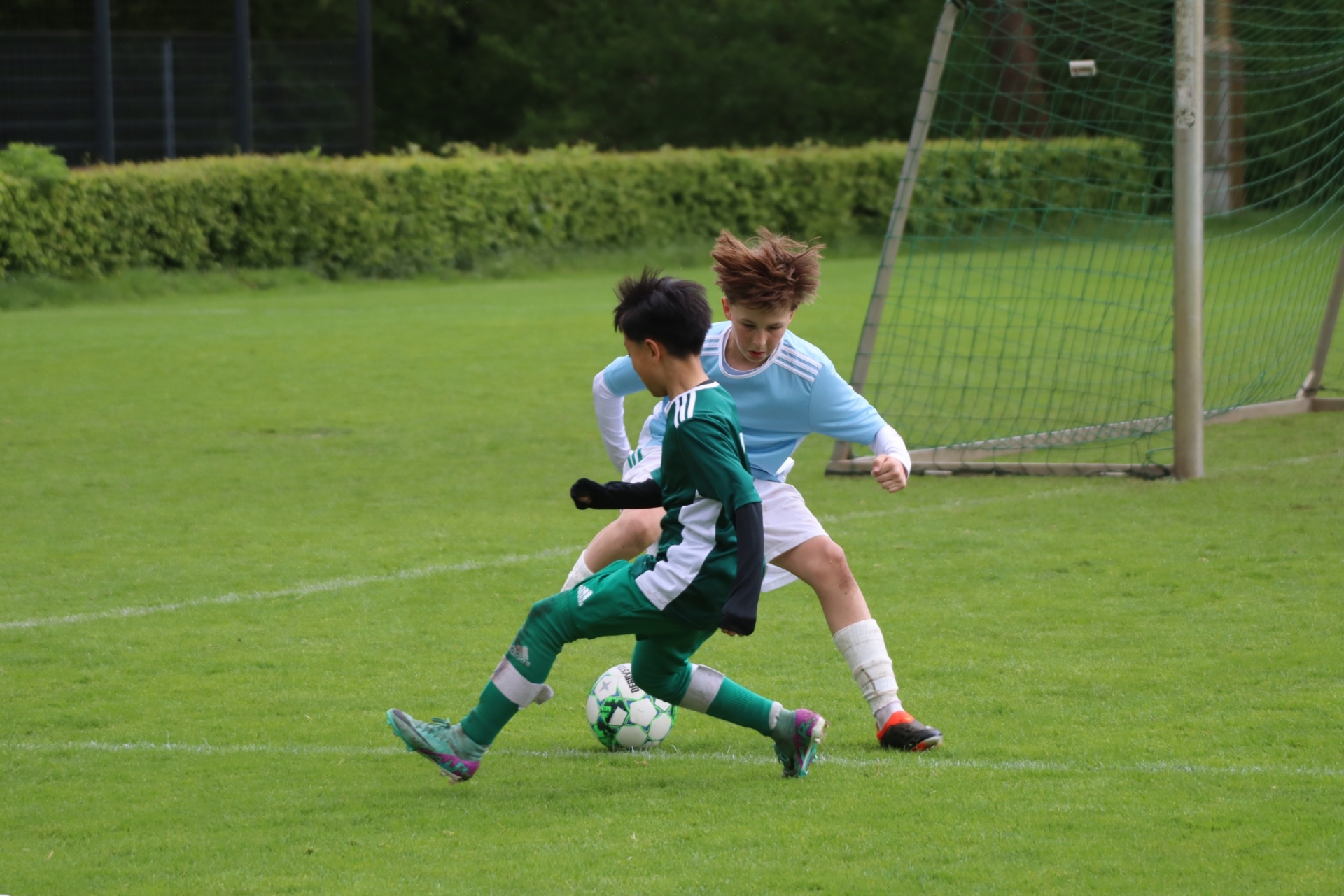 [{"clang_id":1,"value":"Zwei Jugendliche spielen Fußball auf einem Rasenplatz. Ein Spieler in grünem Trikot schießt auf den Ball, der andere in hellem Blau versucht, den Ball zu blocken."}]