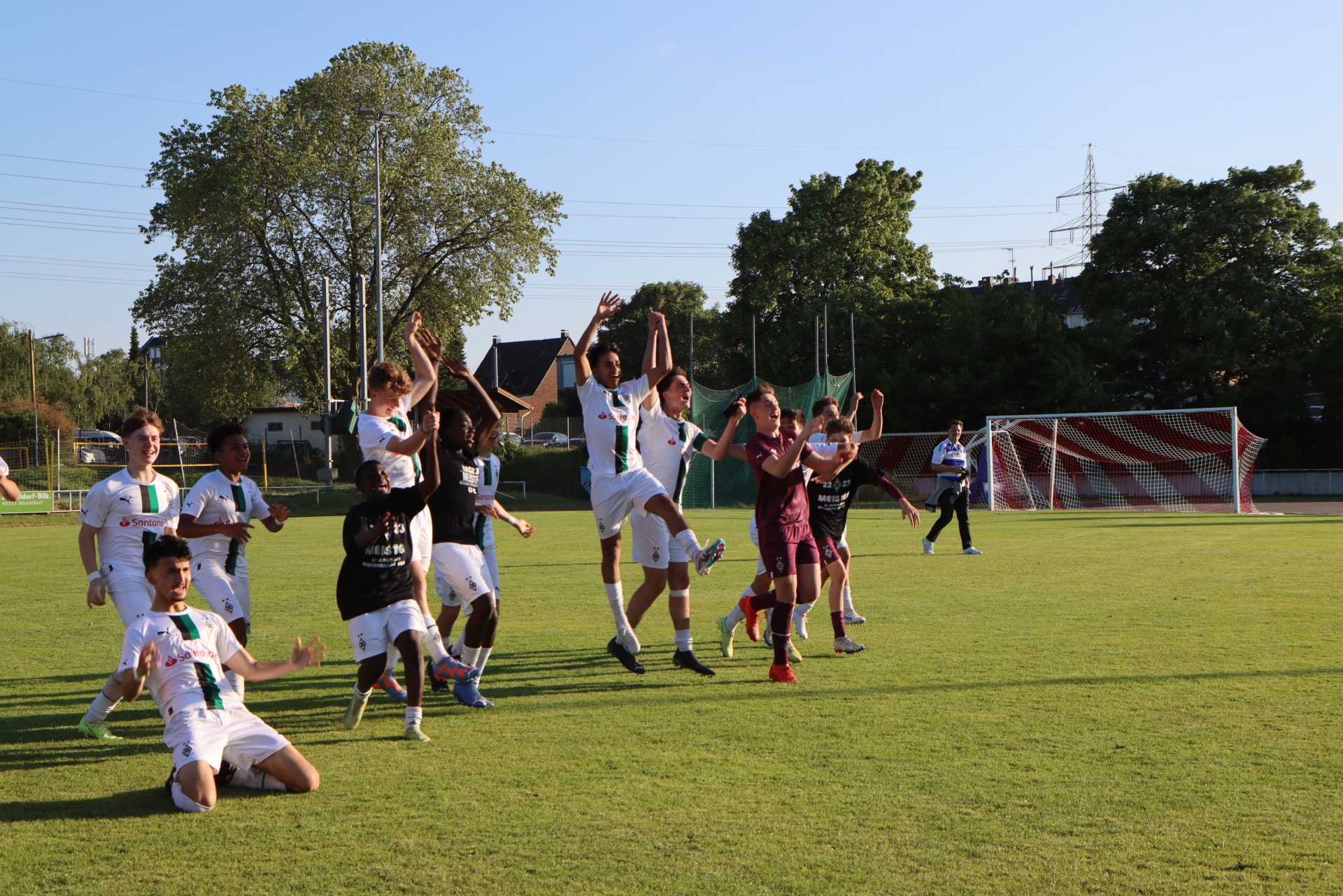 [{"clang_id":1,"value":"Fußballspieler feiern auf grünem Rasen. Einige springen, andere liegen oder stehen. Im Hintergrund Bäume und ein Fußballtor."}]