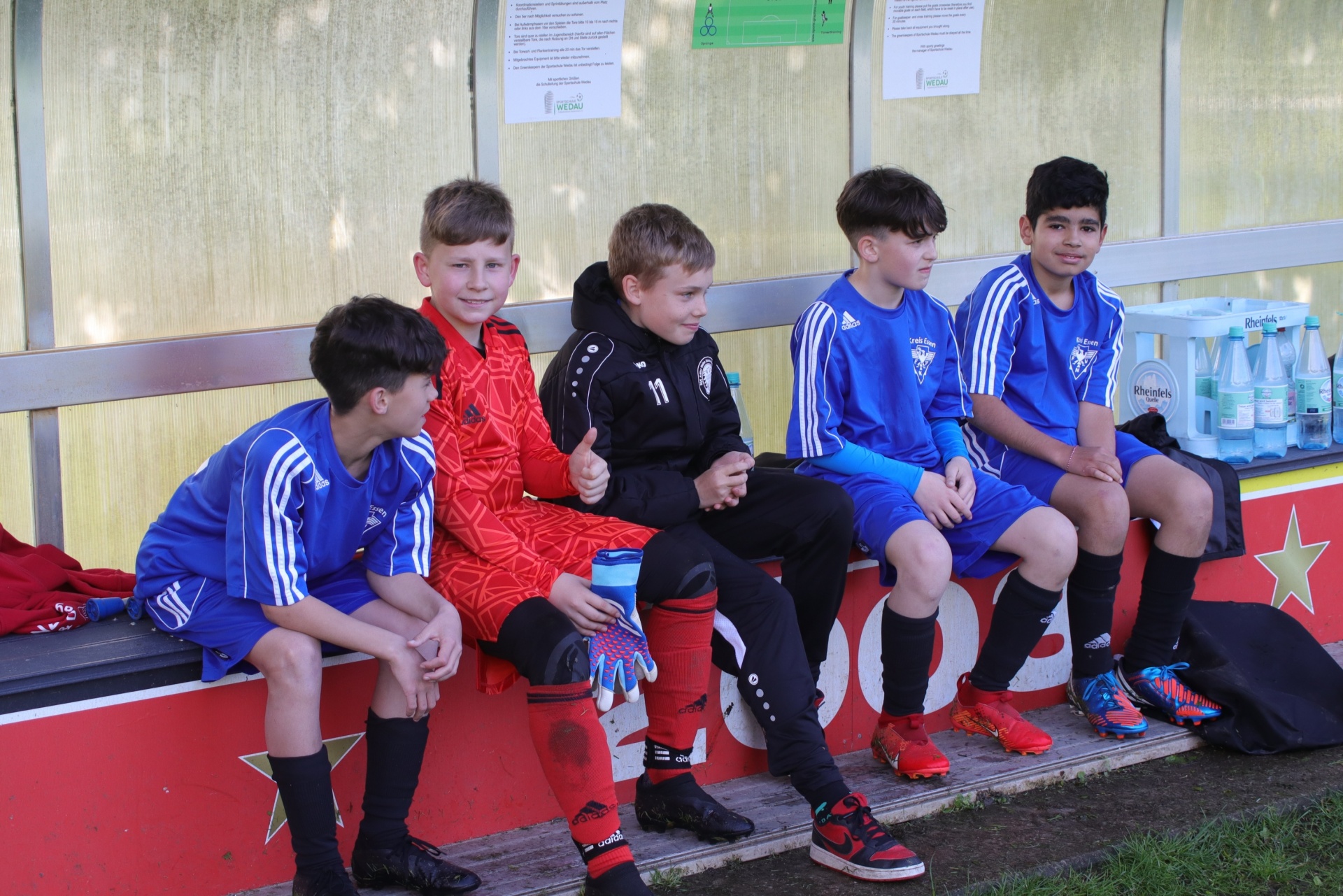 [{"clang_id":1,"value":"Fünf Jungen sitzen auf einer Bank vor einem metallverkleideten Gebäude. Sie tragen blaue oder rote Sportkleidung und Fußballschuhe. Einige haben Trainingsjacken an."}]