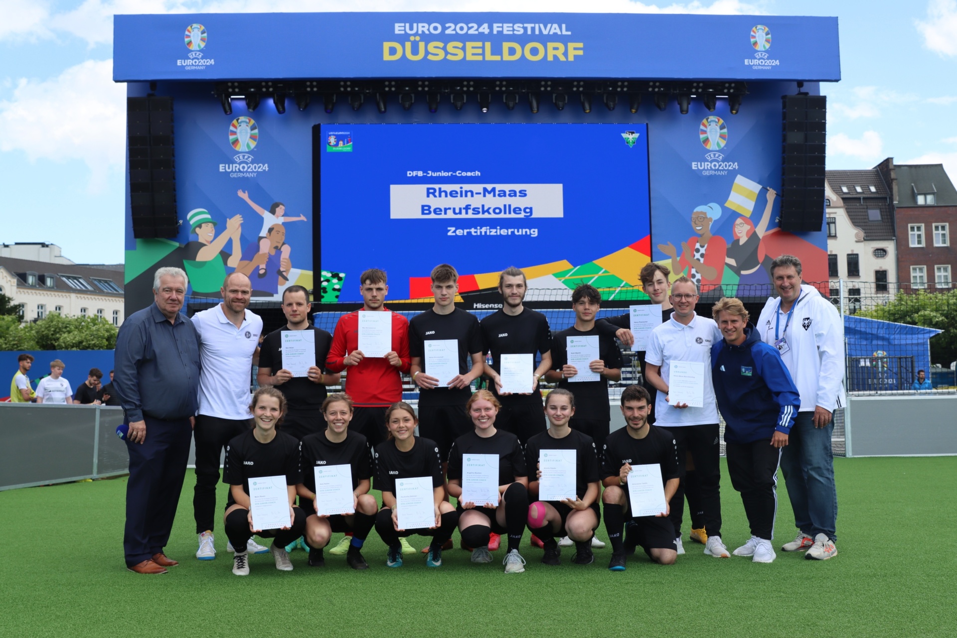 [{"clang_id":1,"value":"Gruppe Jugendlicher mit Zertifikaten vor einer Bühne mit EURO 2024 Logo und dem Text \"Rhein-Maas Berufskolleg Zertifizierung\". Männer stehen seitlich. Rasenfläche im Vordergrund."}]